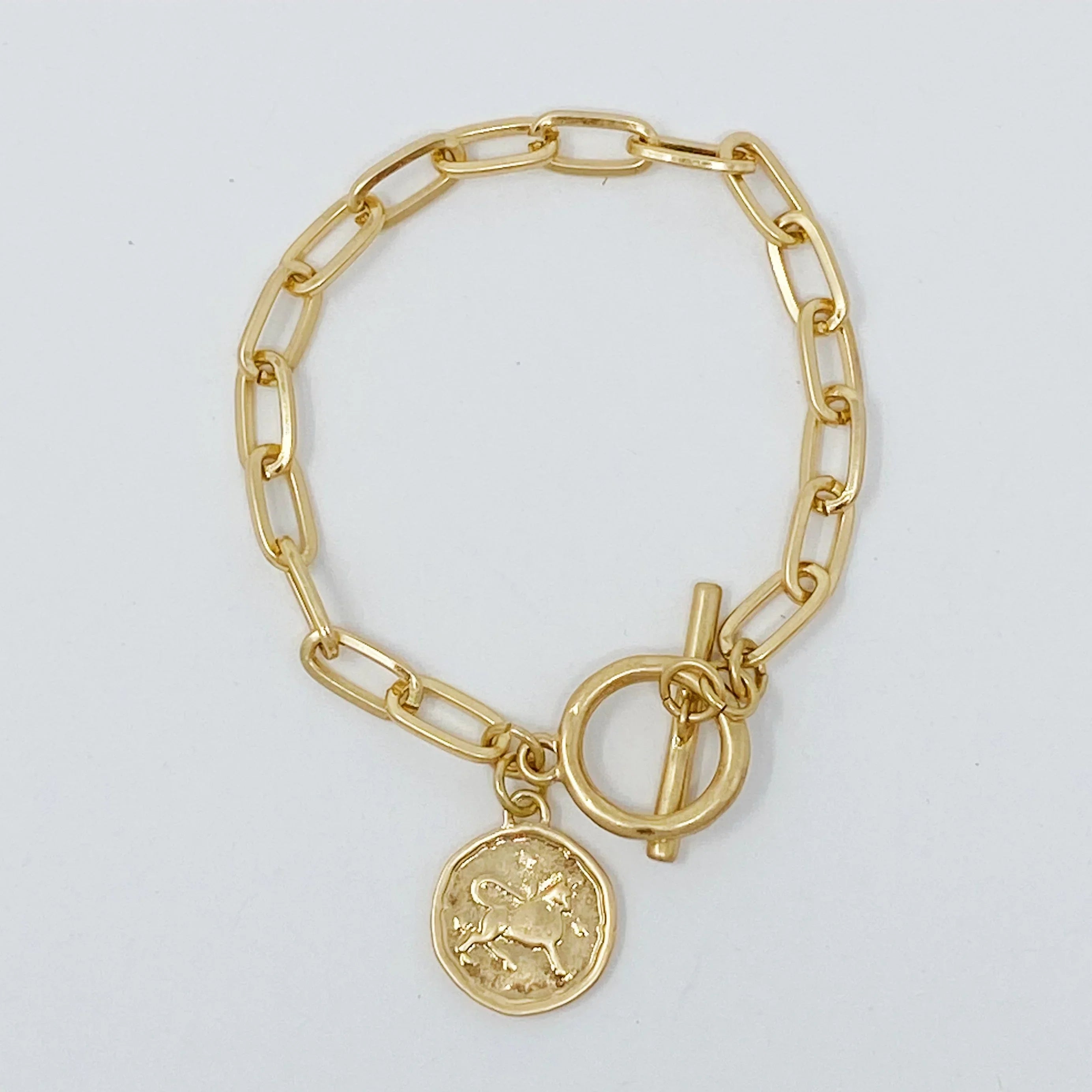 Gold chain bracelet with toggle clasp and round unicorn charm on white background