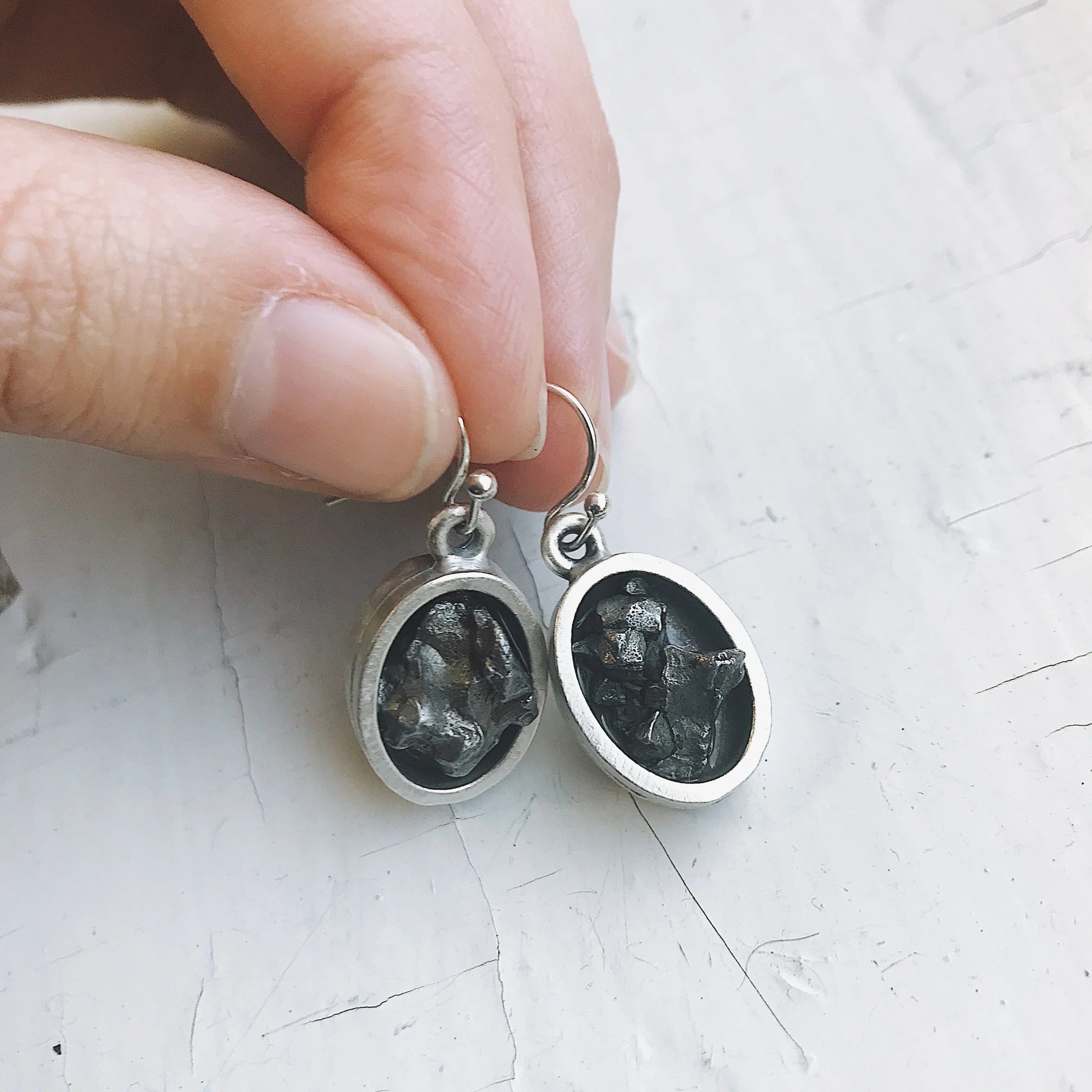 Hand holding artisanal silver earrings with rough black stones, Qu!rk Boutique jewelry