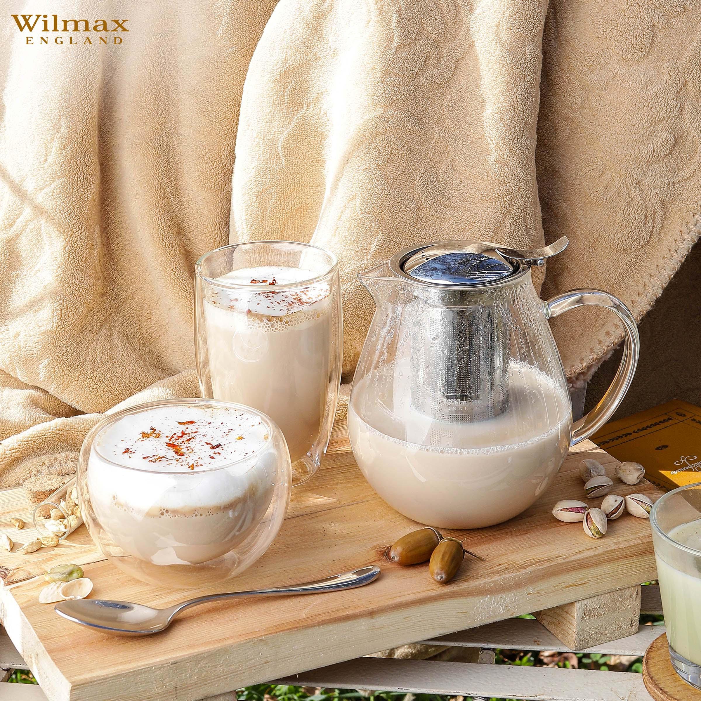 Glass teapot with infuser, two frothy chai lattes, and pistachios on wooden tray, cozy setting