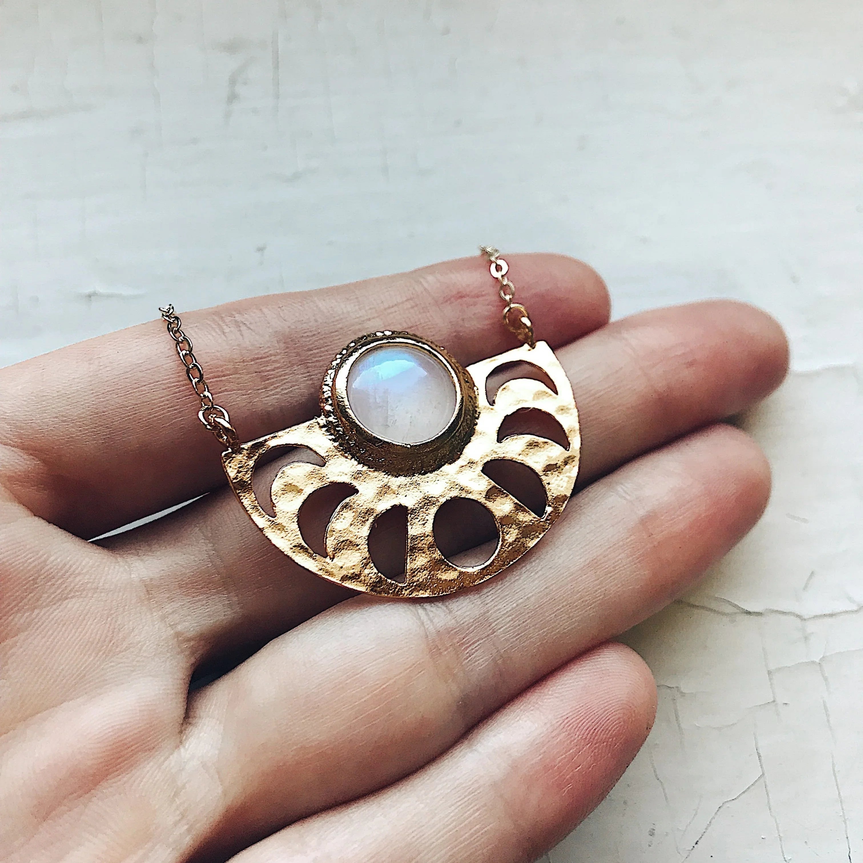 Hand holding gold crescent necklace with moonstone pendant and cutout details