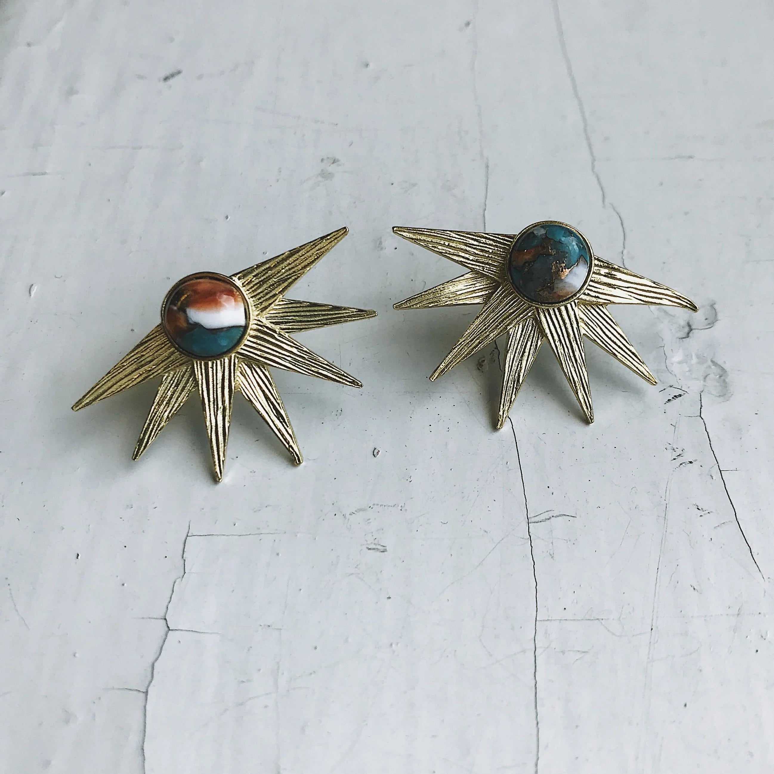 Pair of vintage gold sunburst earrings with multicolor stone centers on cracked concrete surface