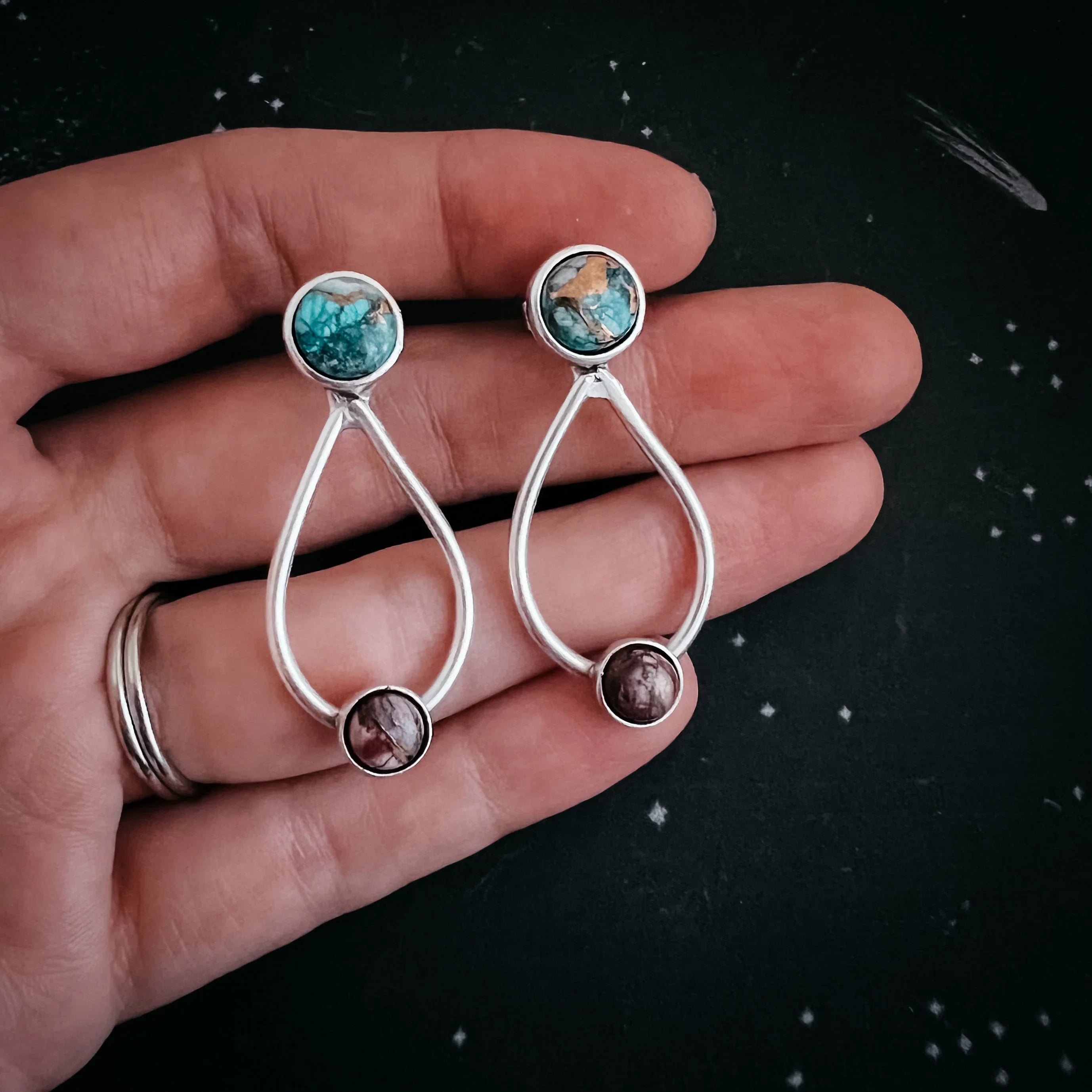Hand holding pair of artist-designed gemstone drop earrings with silver teardrop frames