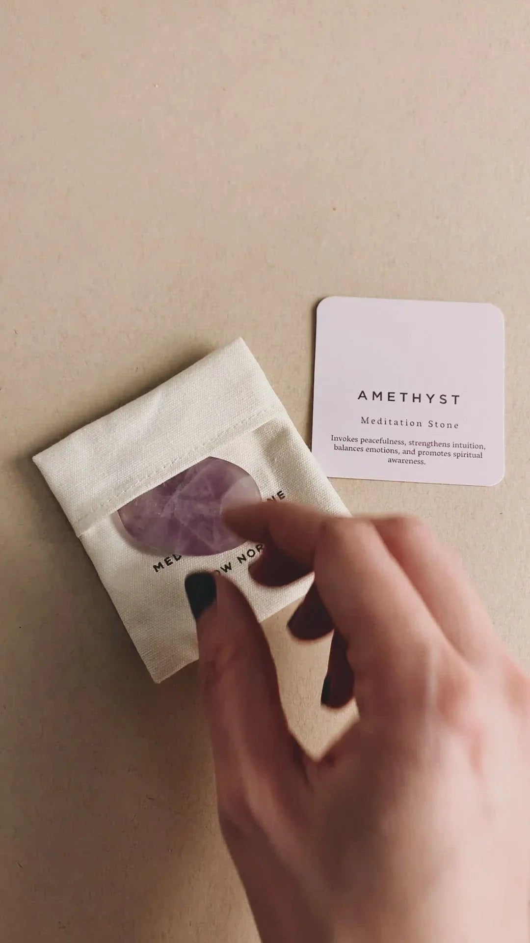 Hand holding amethyst meditation stone next to pouch and card detailing its spiritual benefits