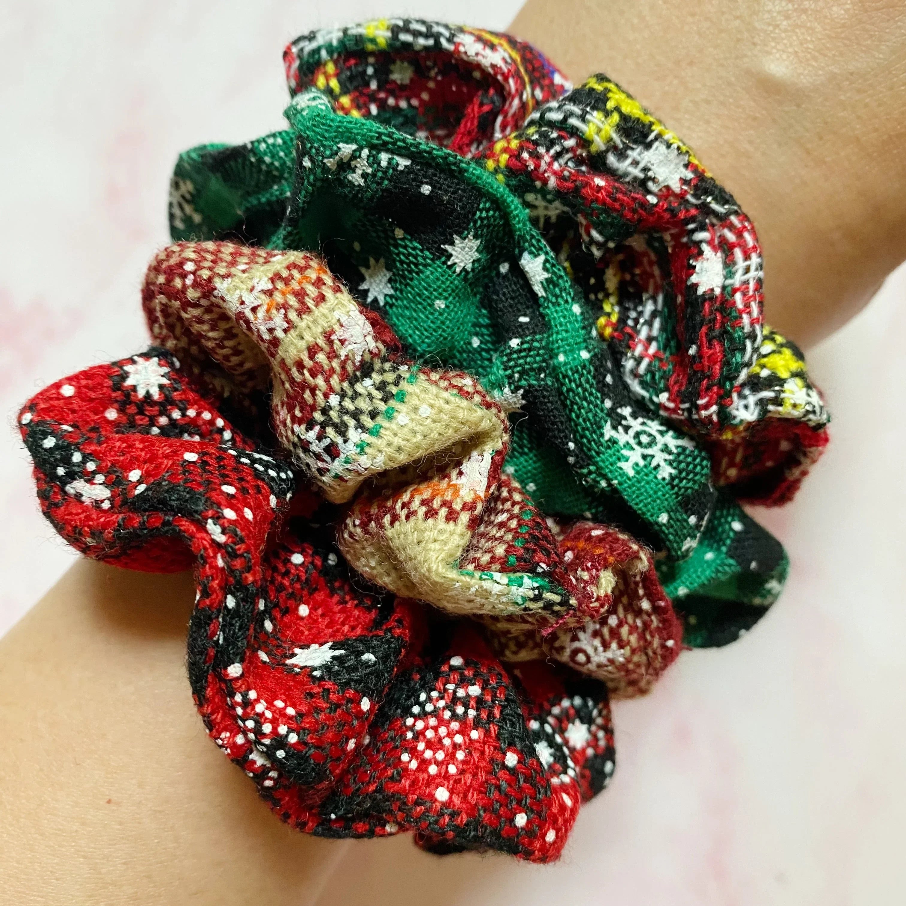 Close-up of multicolored plaid fabric scrunchies with star and snowflake patterns on wrist