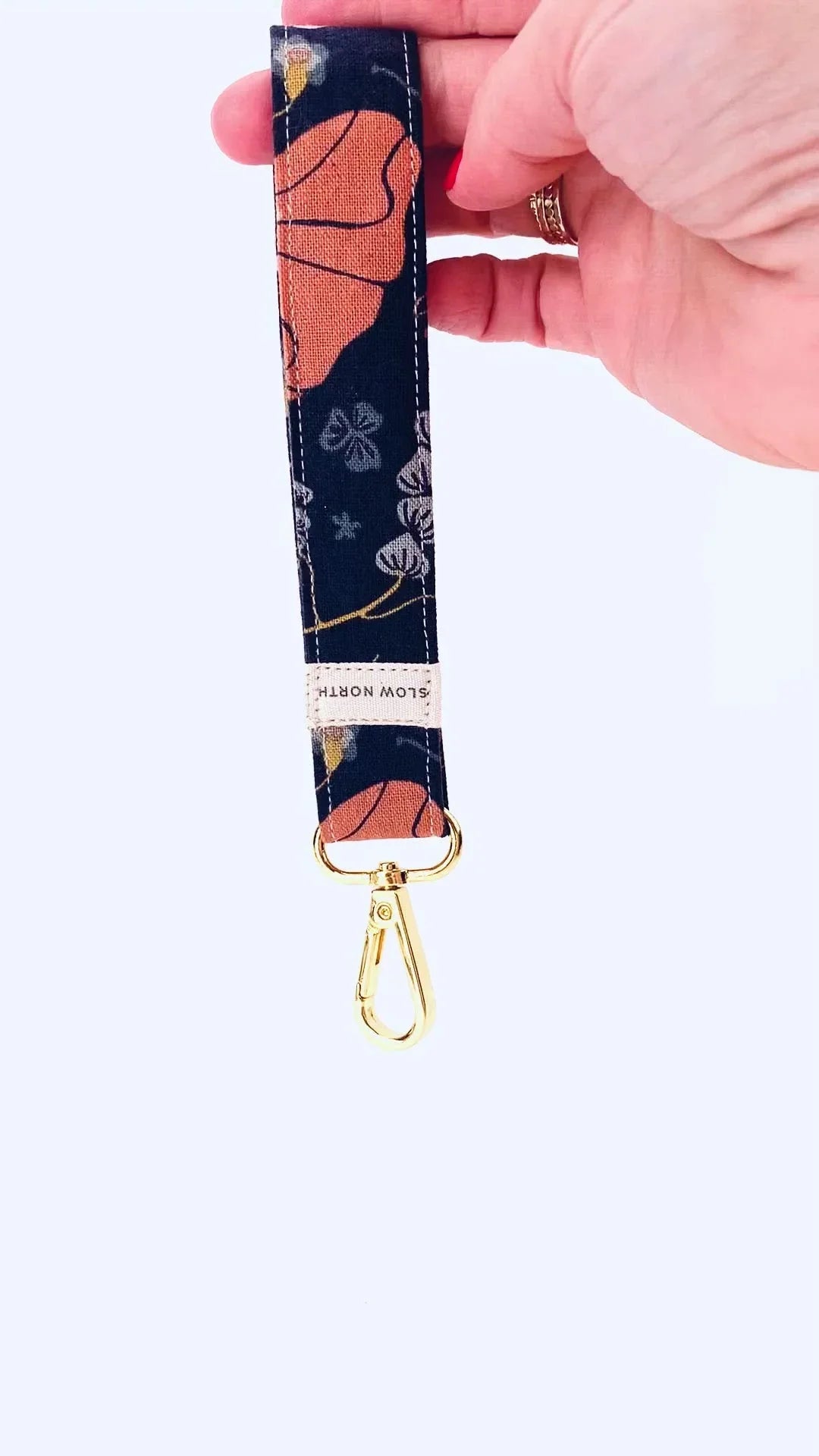Hand holding floral fabric keychain with gold clasp and Slow North label