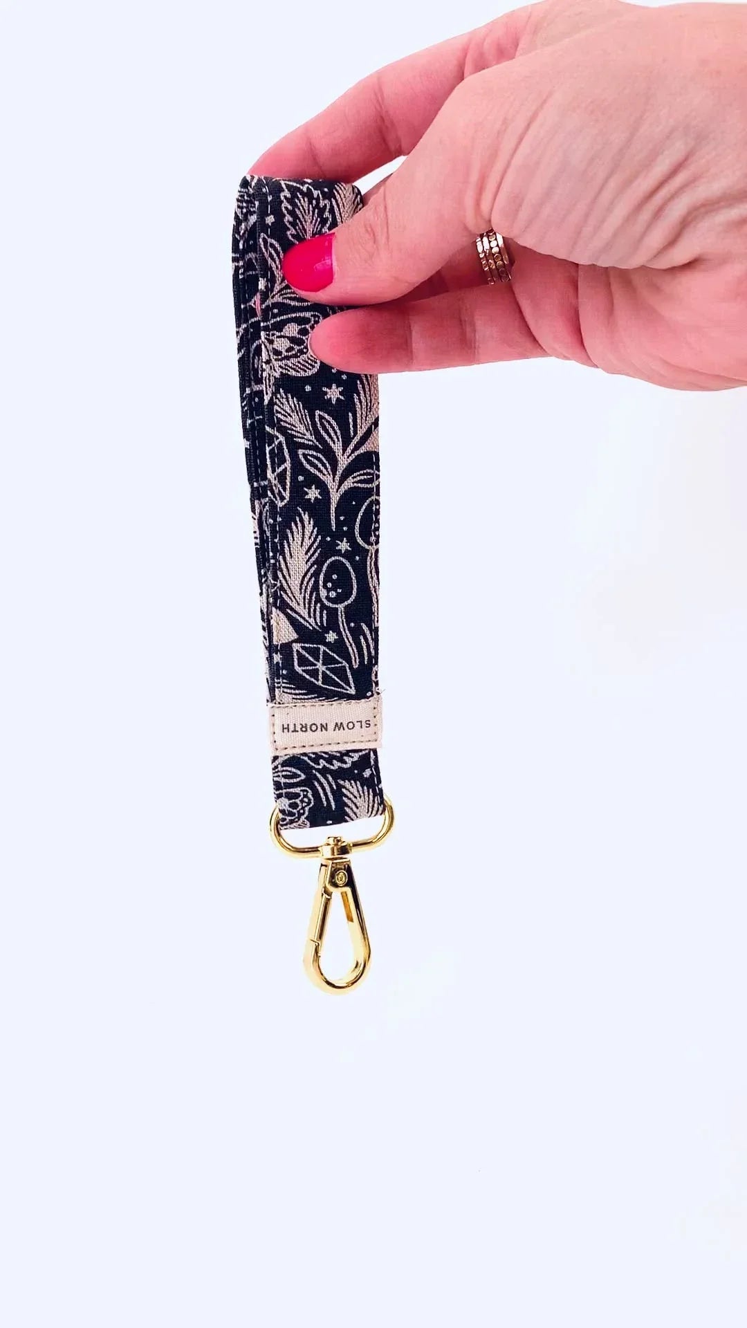 Hand holding a navy blue fabric keychain with white floral patterns and gold metal clip