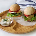 Two veggie burgers with lettuce, tomato, and cheese on a wooden tray with herb dip, artisan style