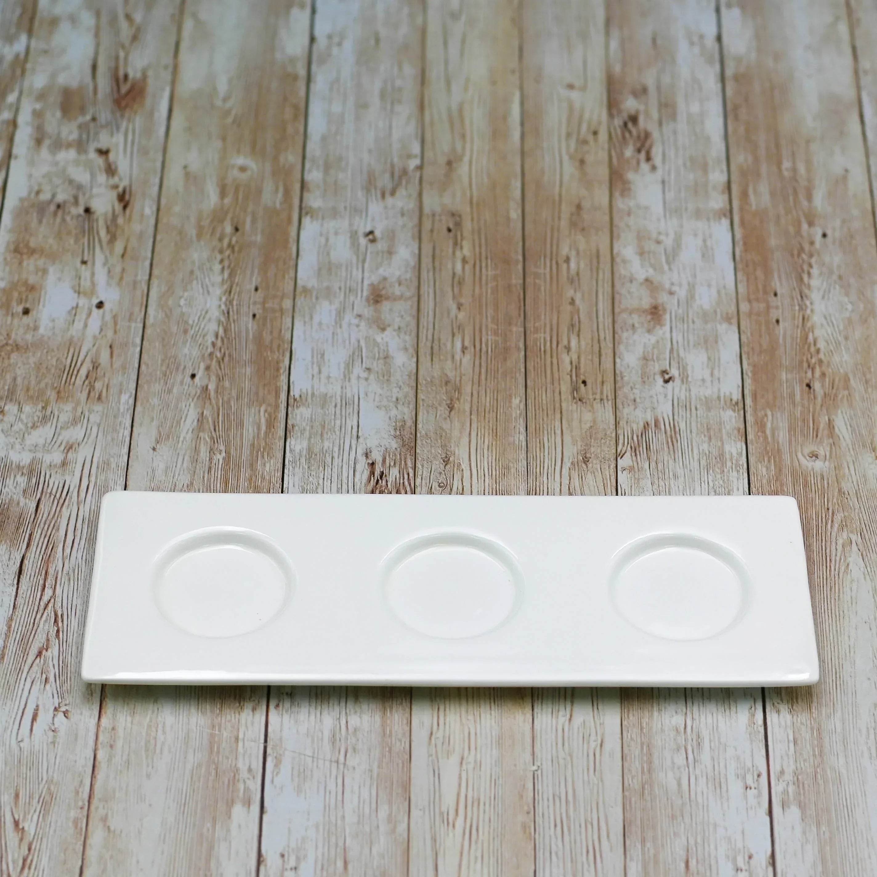White rectangular ceramic tray with three round indentations on wooden surface
