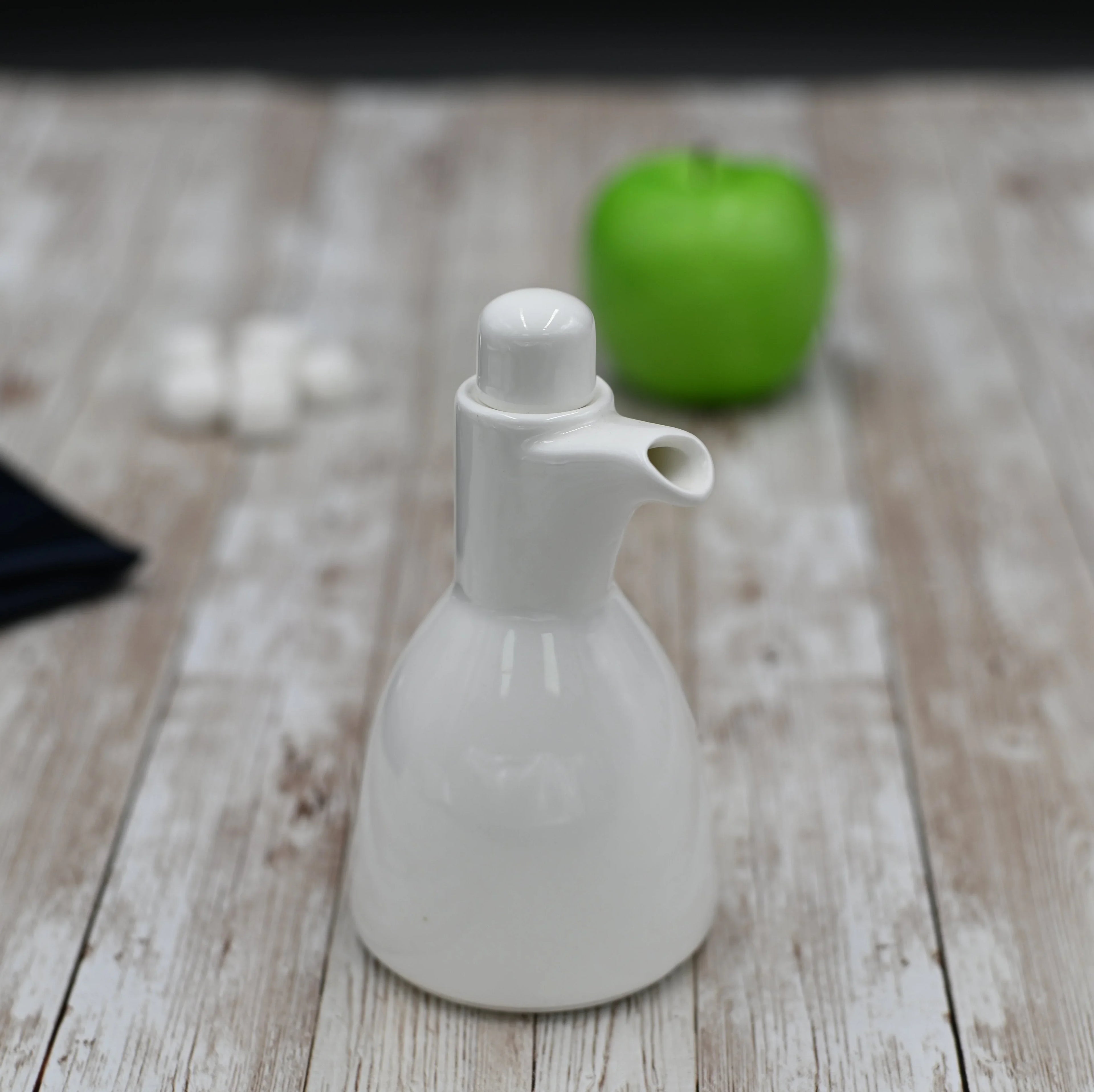 Modern white ceramic oil bottle on rustic wood table, green apple in background, Qu!rk Boutique style