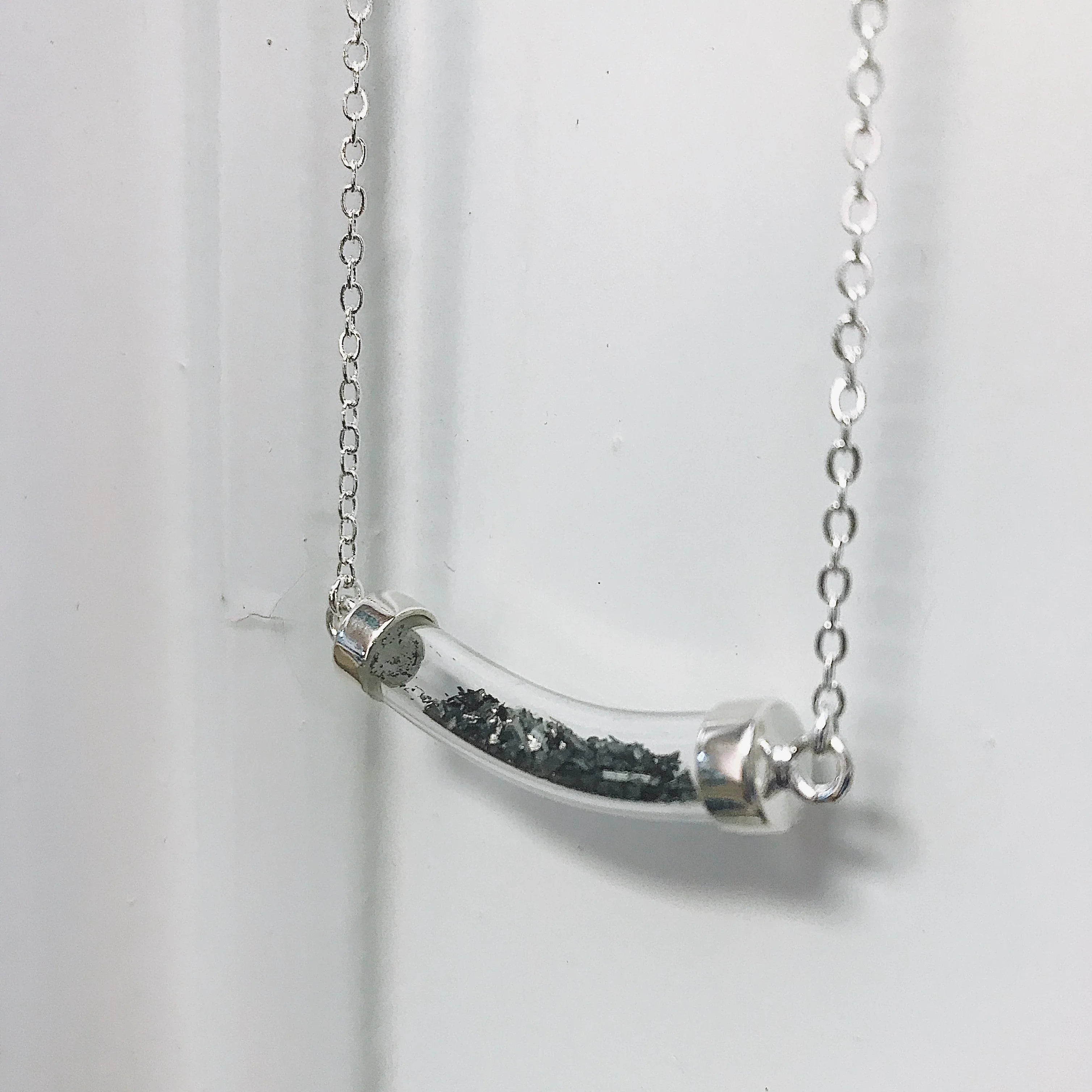Silver chain necklace with a curved glass pendant containing small black granules