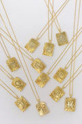 Gold zodiac sign pendant necklaces with sunburst design on white background