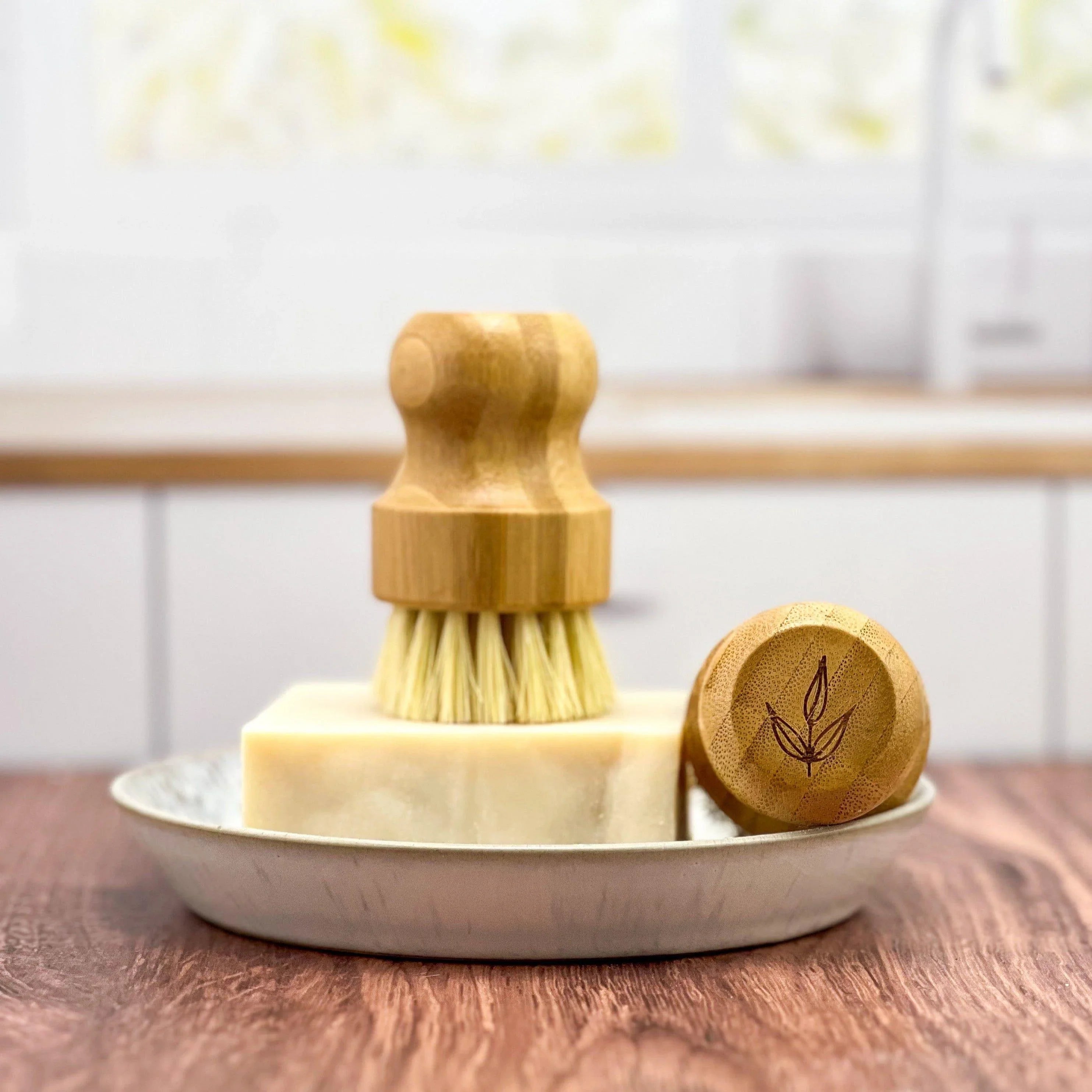 Eco-friendly bamboo scrub brush and bar soap on a dish in a bright kitchen setting