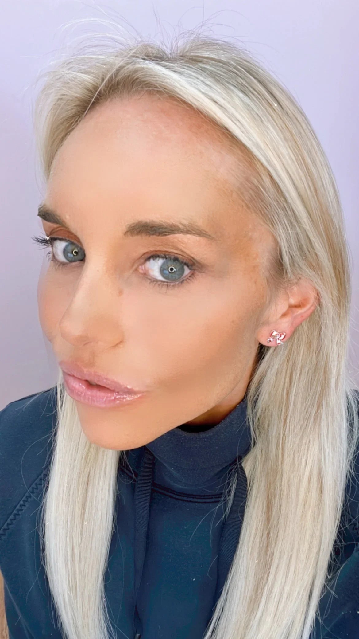 Close-up portrait of a blonde woman with blue eyes wearing pink bow-shaped earrings and a black top