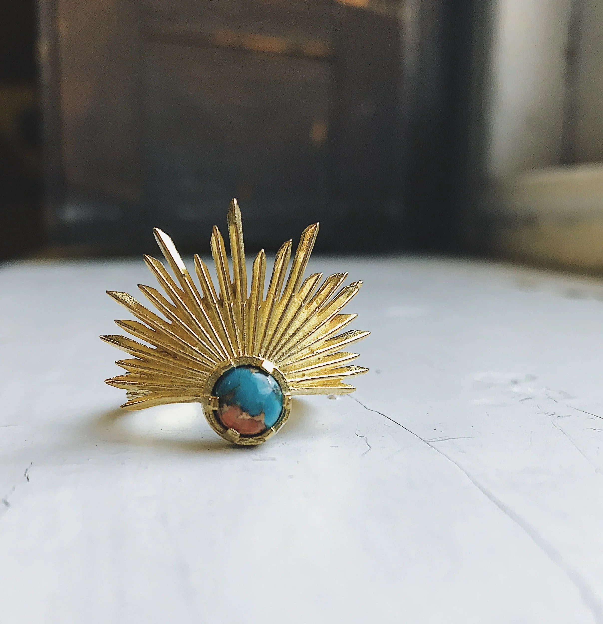Gold sunburst ring with turquoise stone on white surface, artist-designed jewelry at Qu!rk Boutique