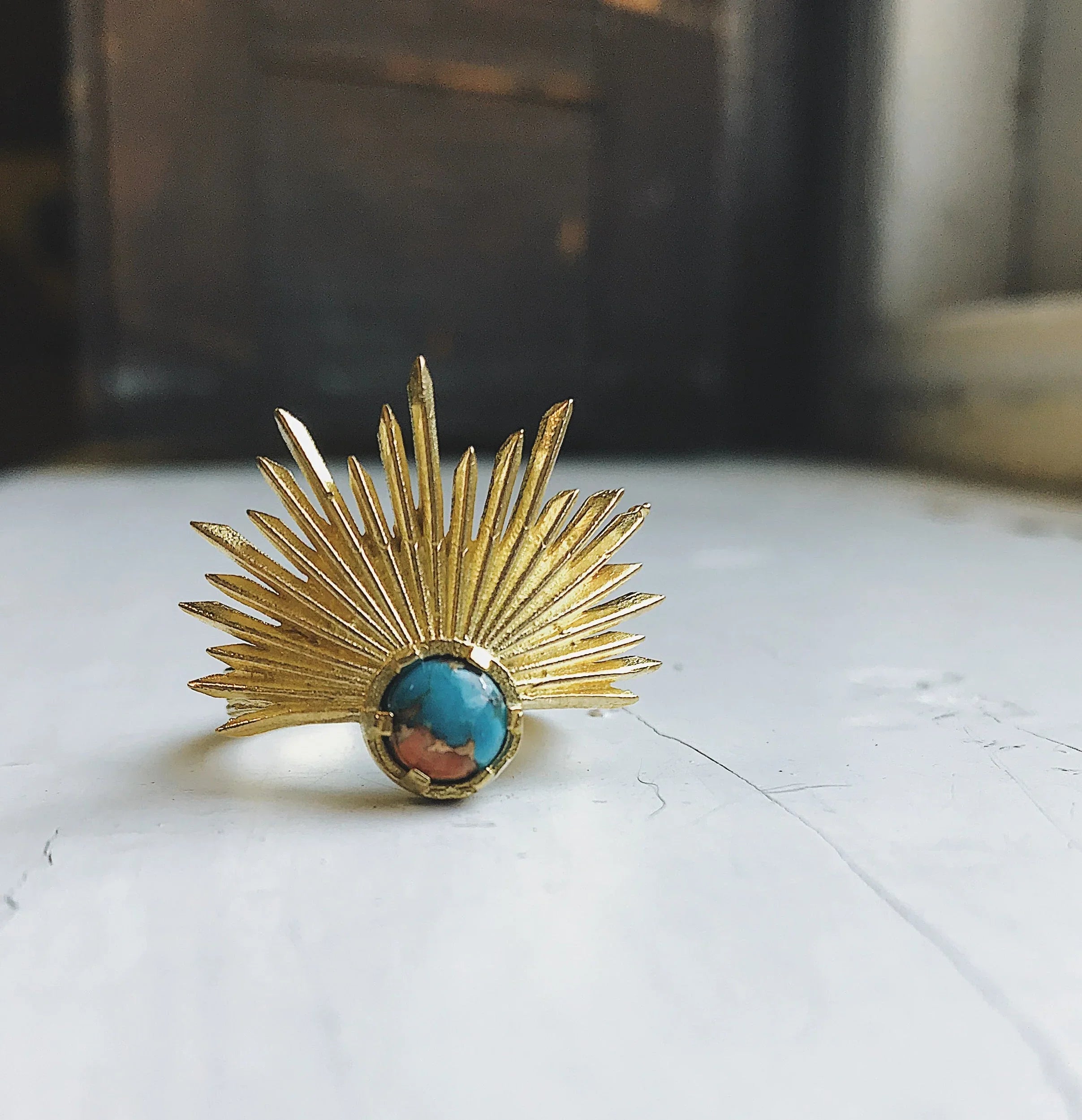 Gold sunburst ring with blue and brown stone set on white surface