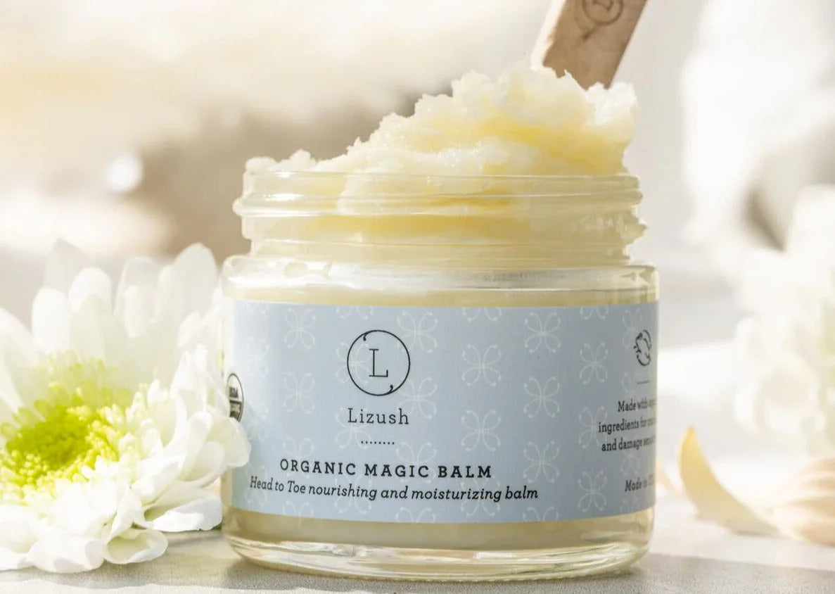 Lizush Organic Magic Balm jar with nourishing moisturizing balm and white flowers on light background