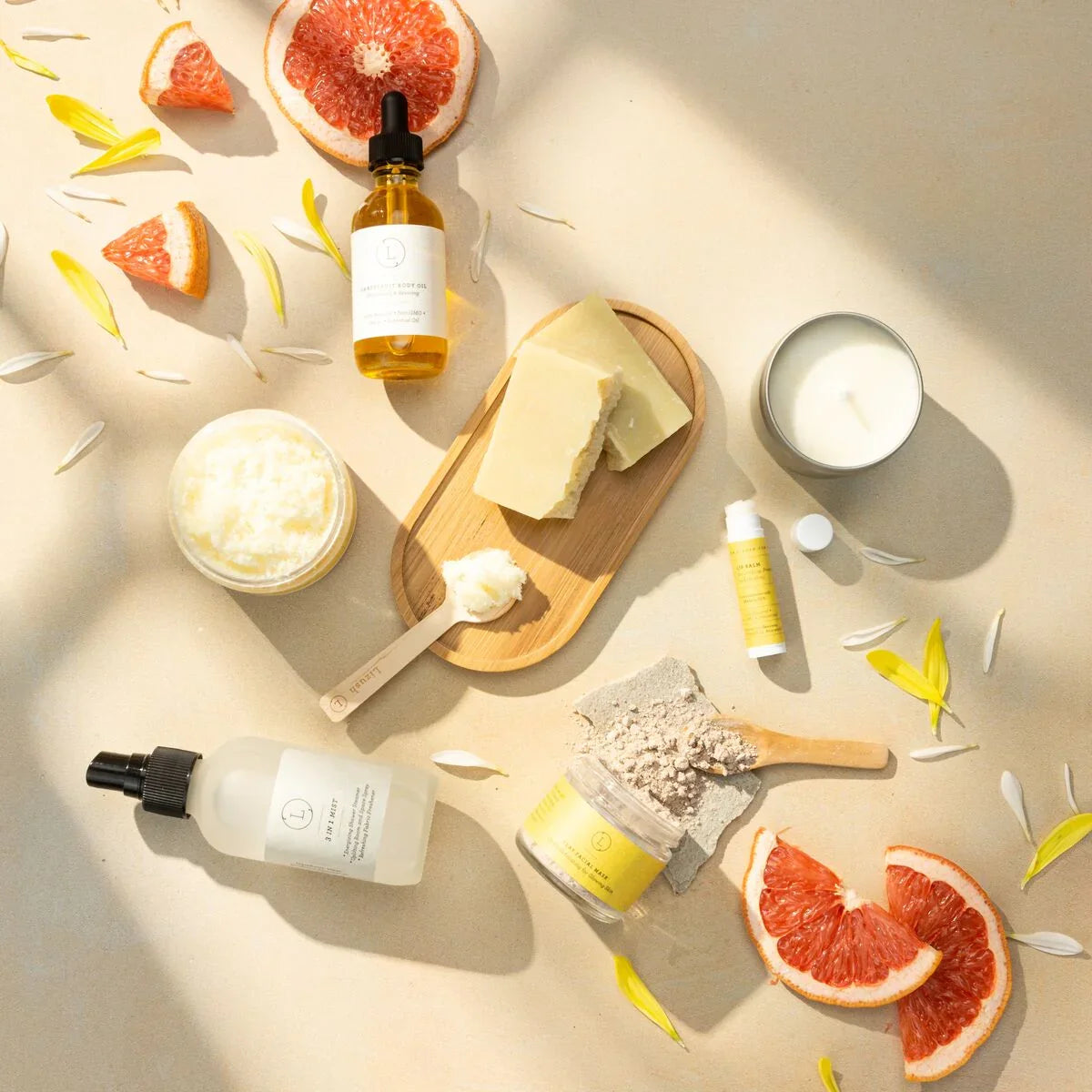 Natural skincare products with grapefruit slices, body oil, balm, whipped cream, soap bars, and candle on beige background