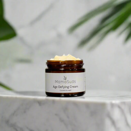 MamaSuds Age Defying Cream in brown glass jar on marble surface with leafy background, Qu!rk Boutique