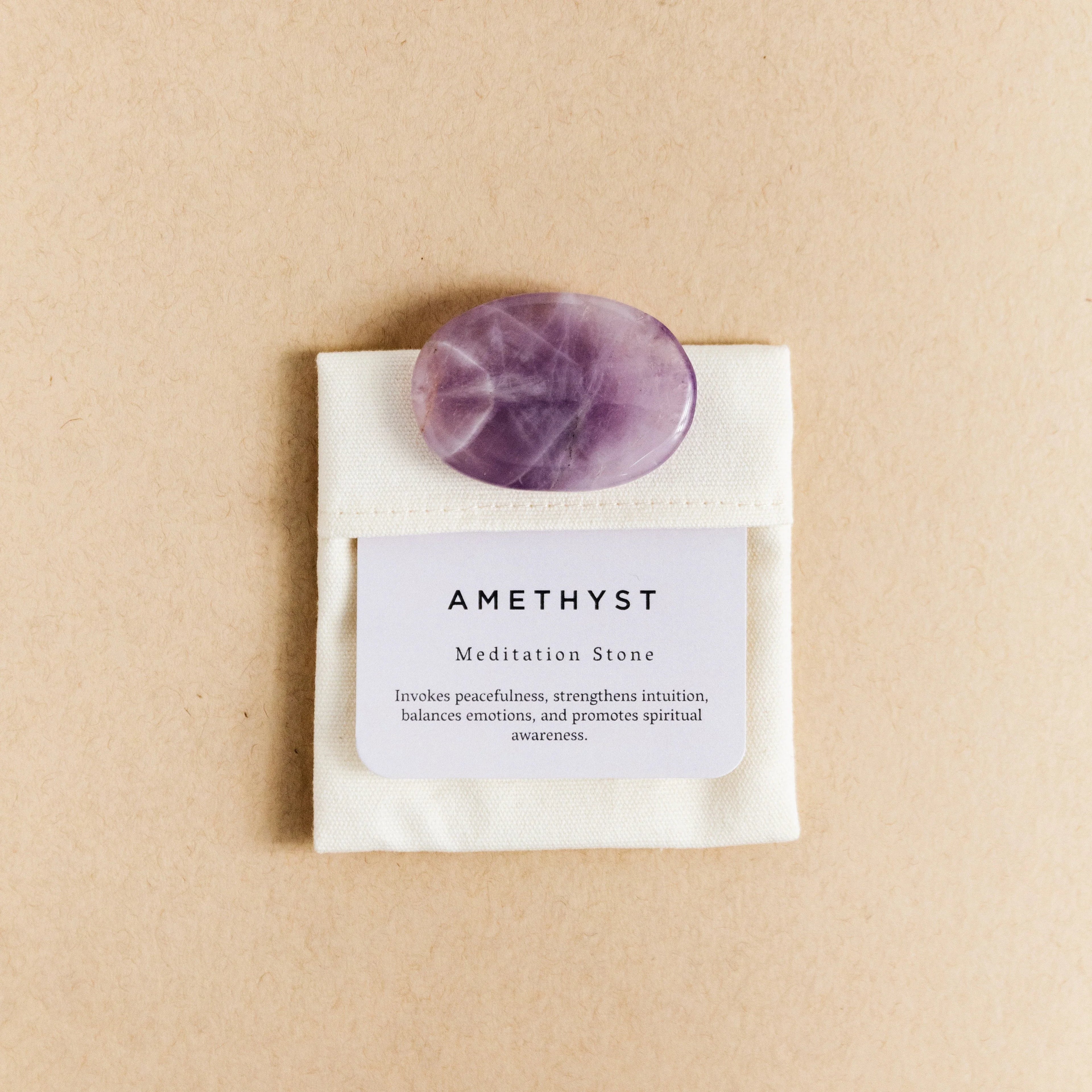 Polished amethyst meditation stone on white pouch with description card on beige background