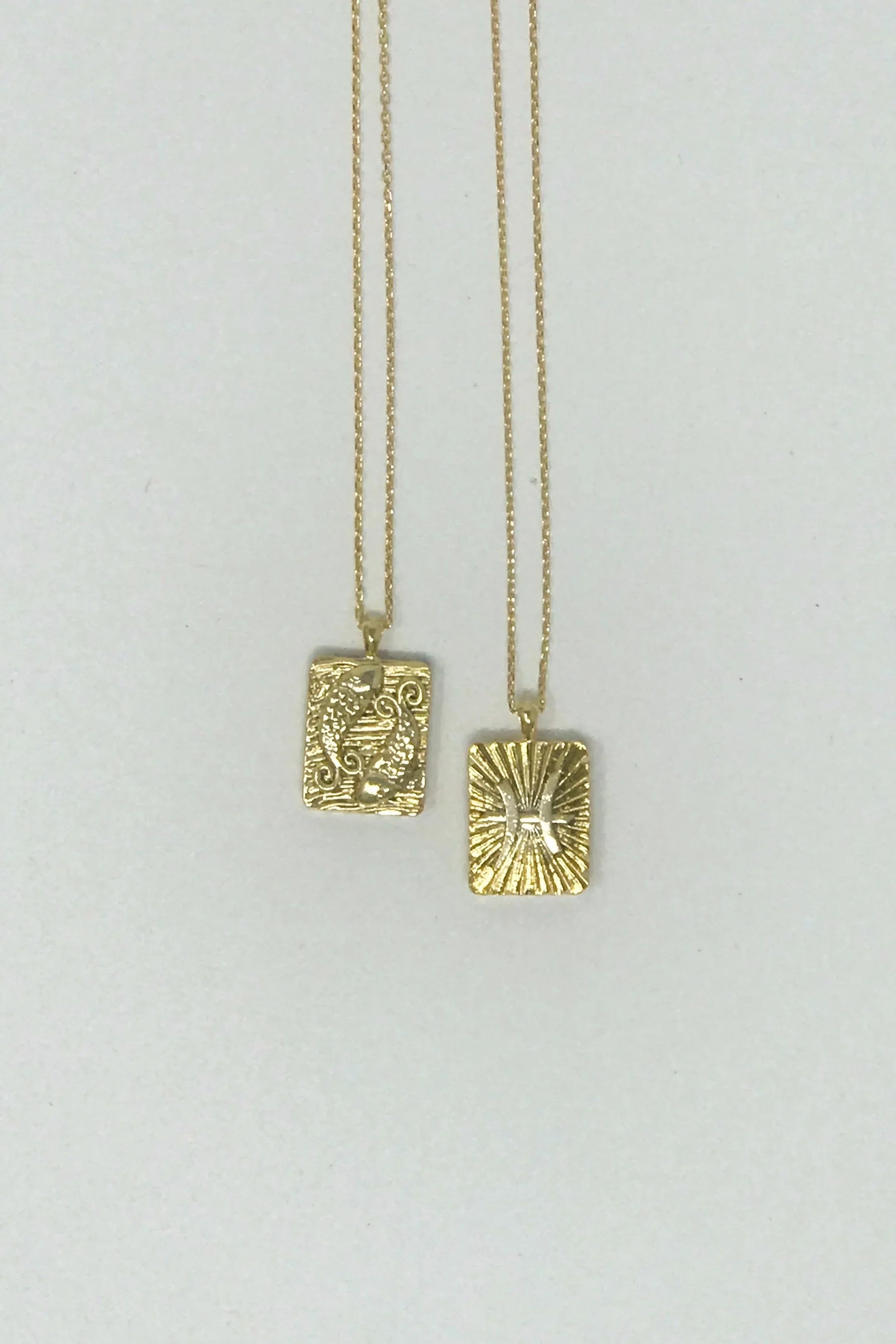 Two gold rectangular pendant necklaces with intricate embossed designs on gold chains