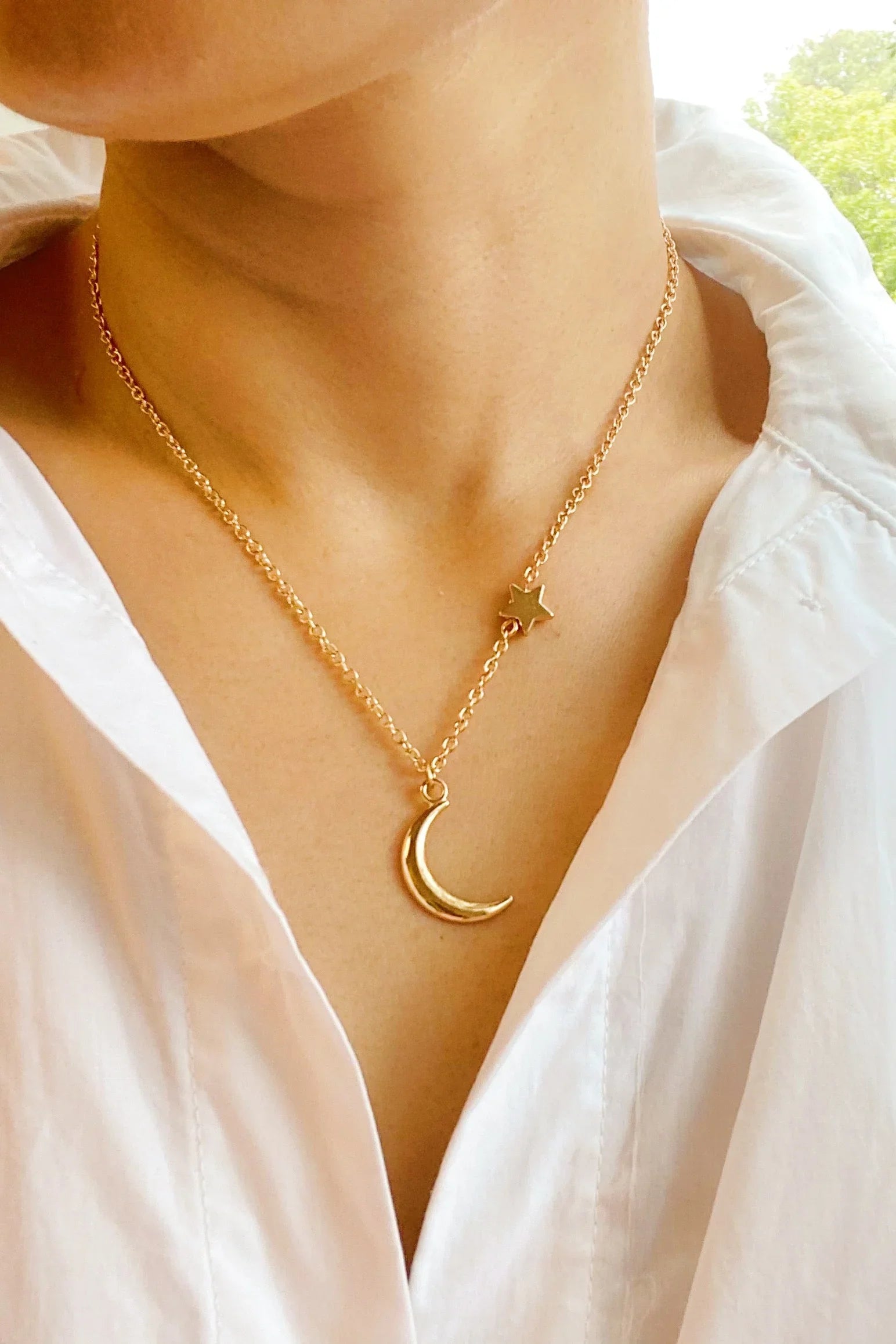 Gold necklace with crescent moon and star charms worn on neck with white collared shirt