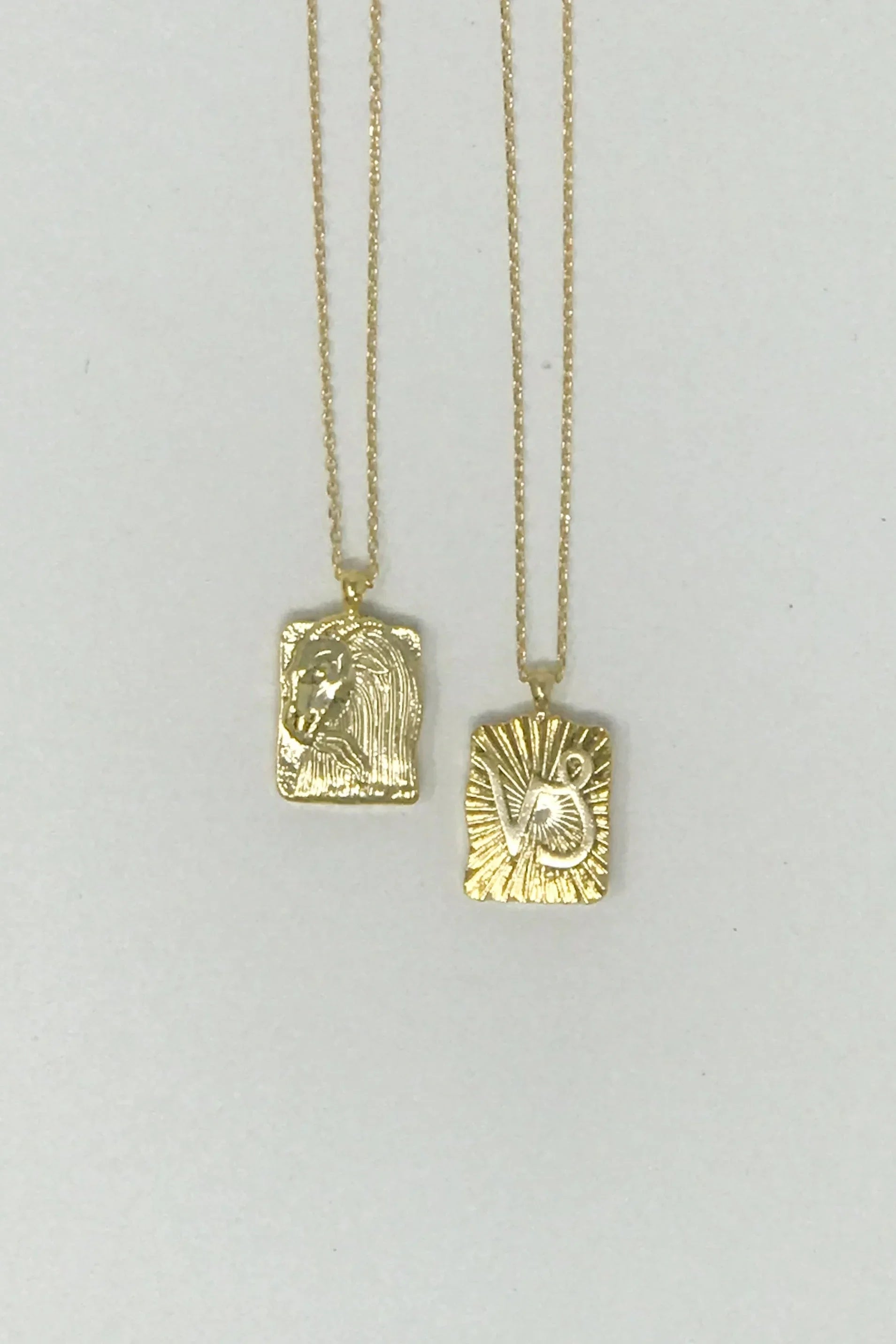 Two gold pendant necklaces with rectangular charms featuring horse head and sunburst designs
