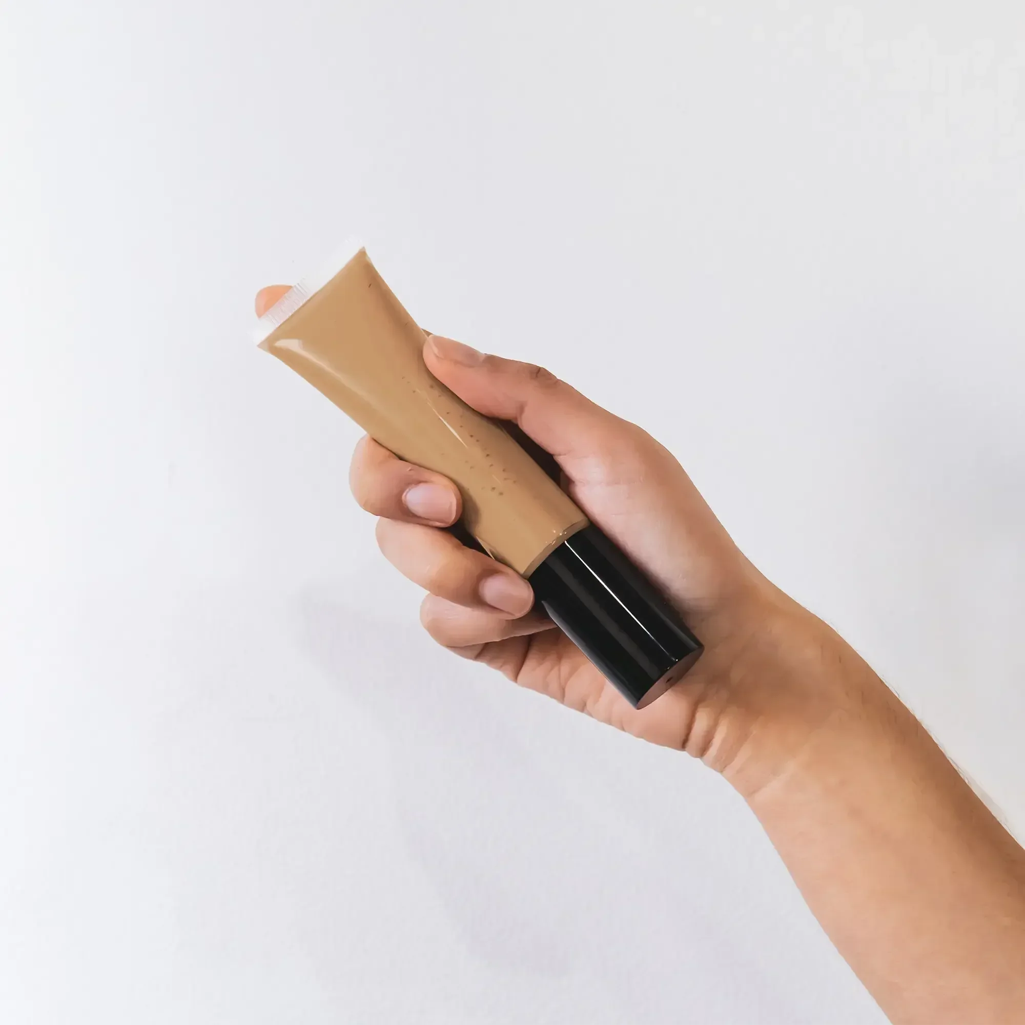 Hand holding a tan BB cream tube with black cap against white background at Qu!rk Boutique