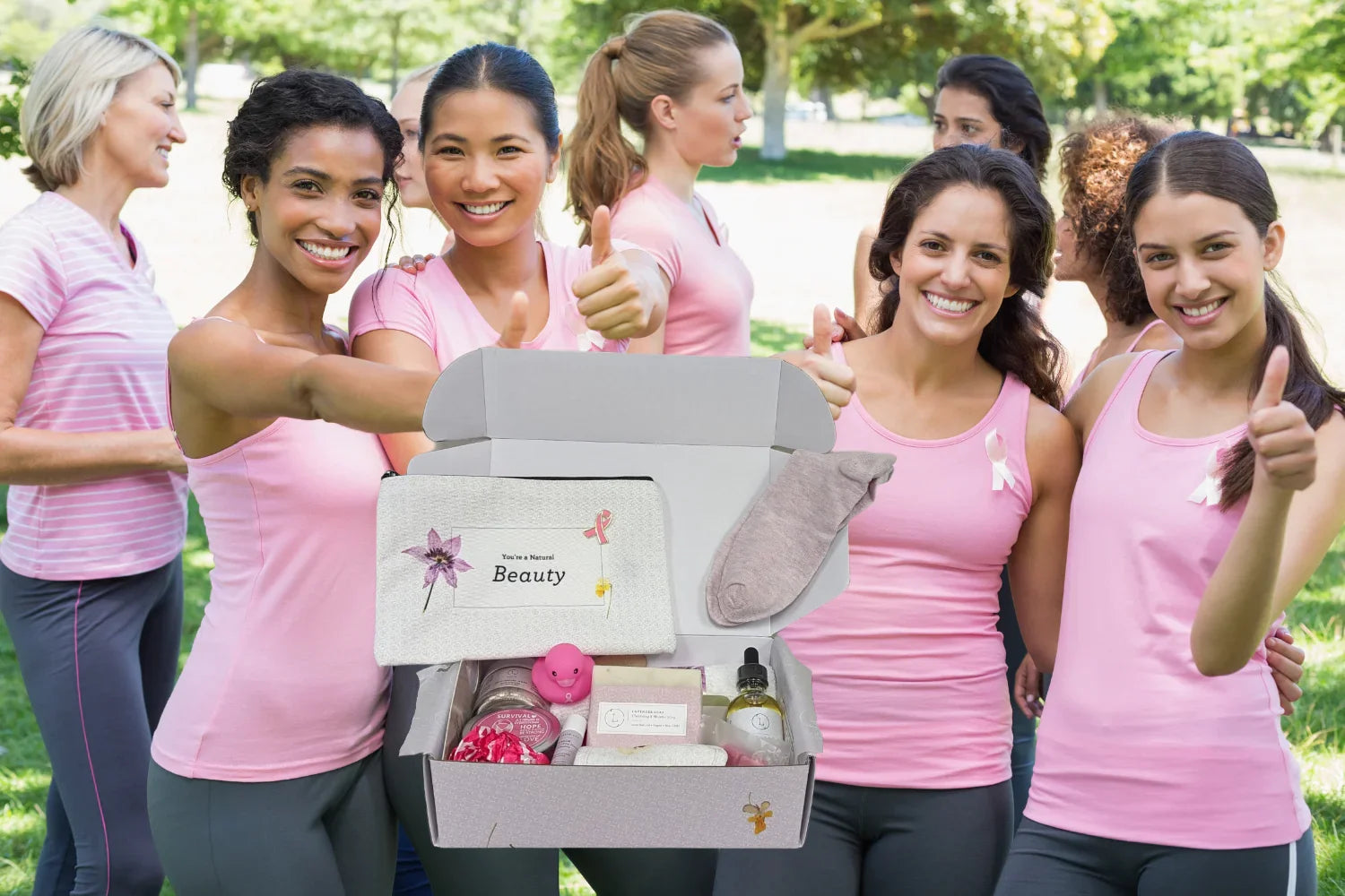 Group of women in pink shirts showing thumbs up around breast cancer awareness gift box outdoors