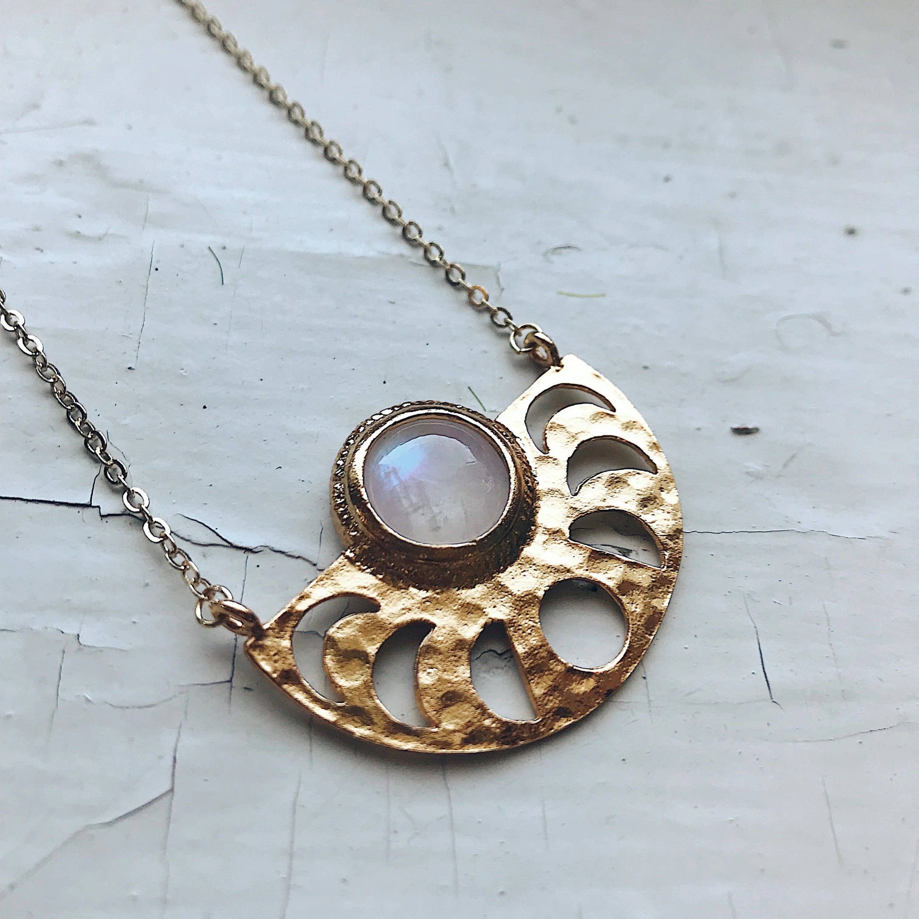 Gold crescent moon necklace with translucent white stone on chain, displayed on cracked white surface