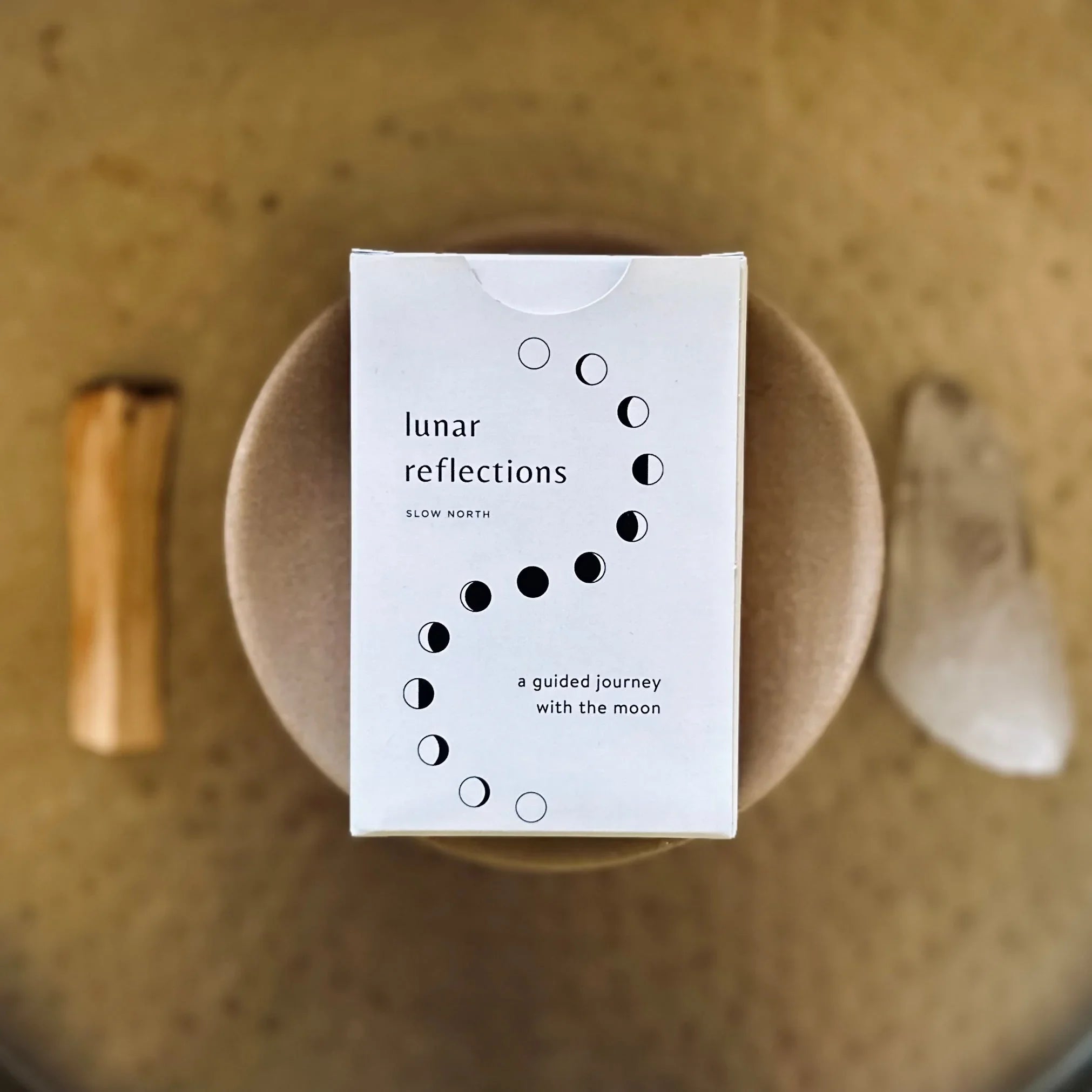 Lunar Reflections box by Slow North with moon phases design on a round cushion, earth-toned background