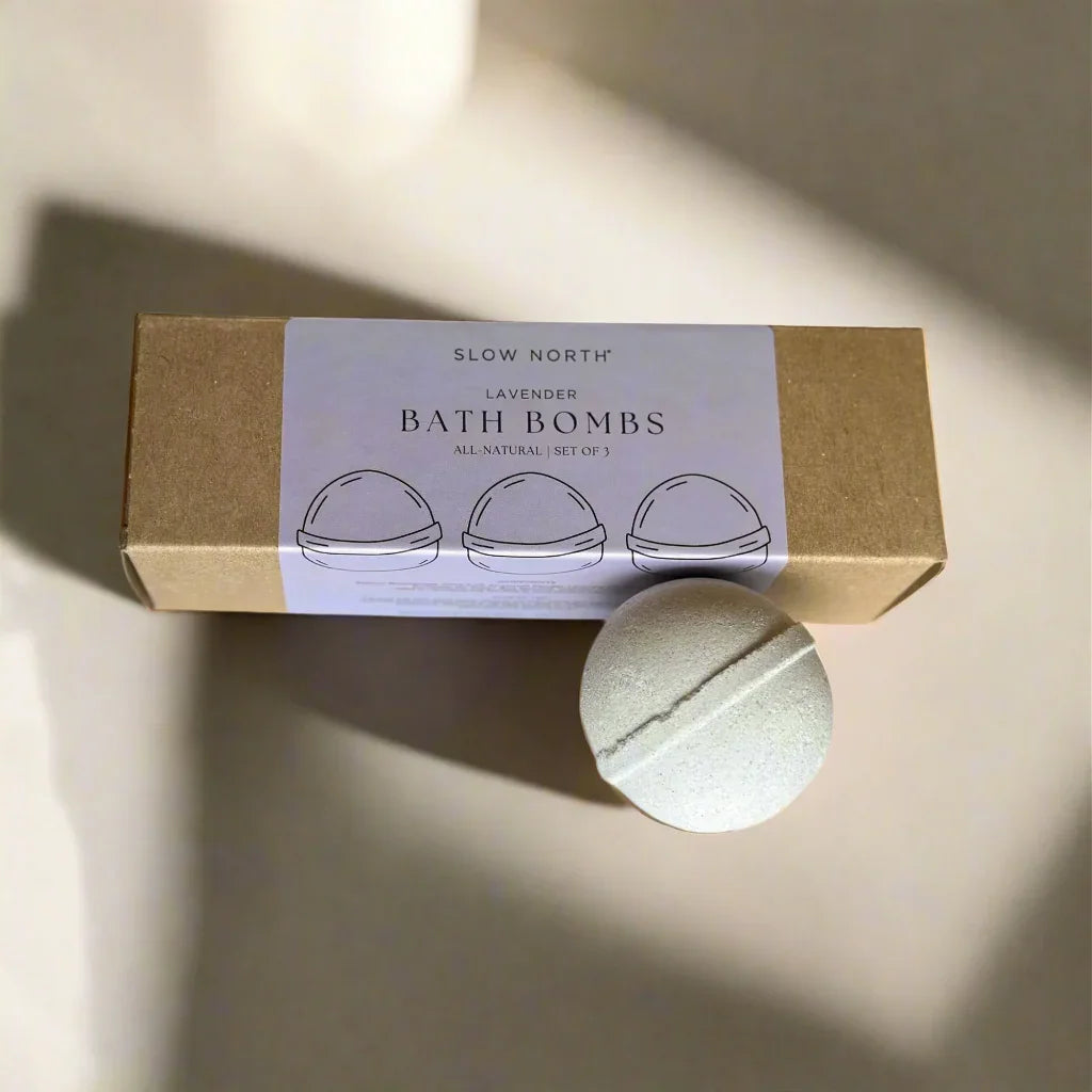 Slow North lavender bath bombs set in kraft paper box with one round bath bomb on beige surface