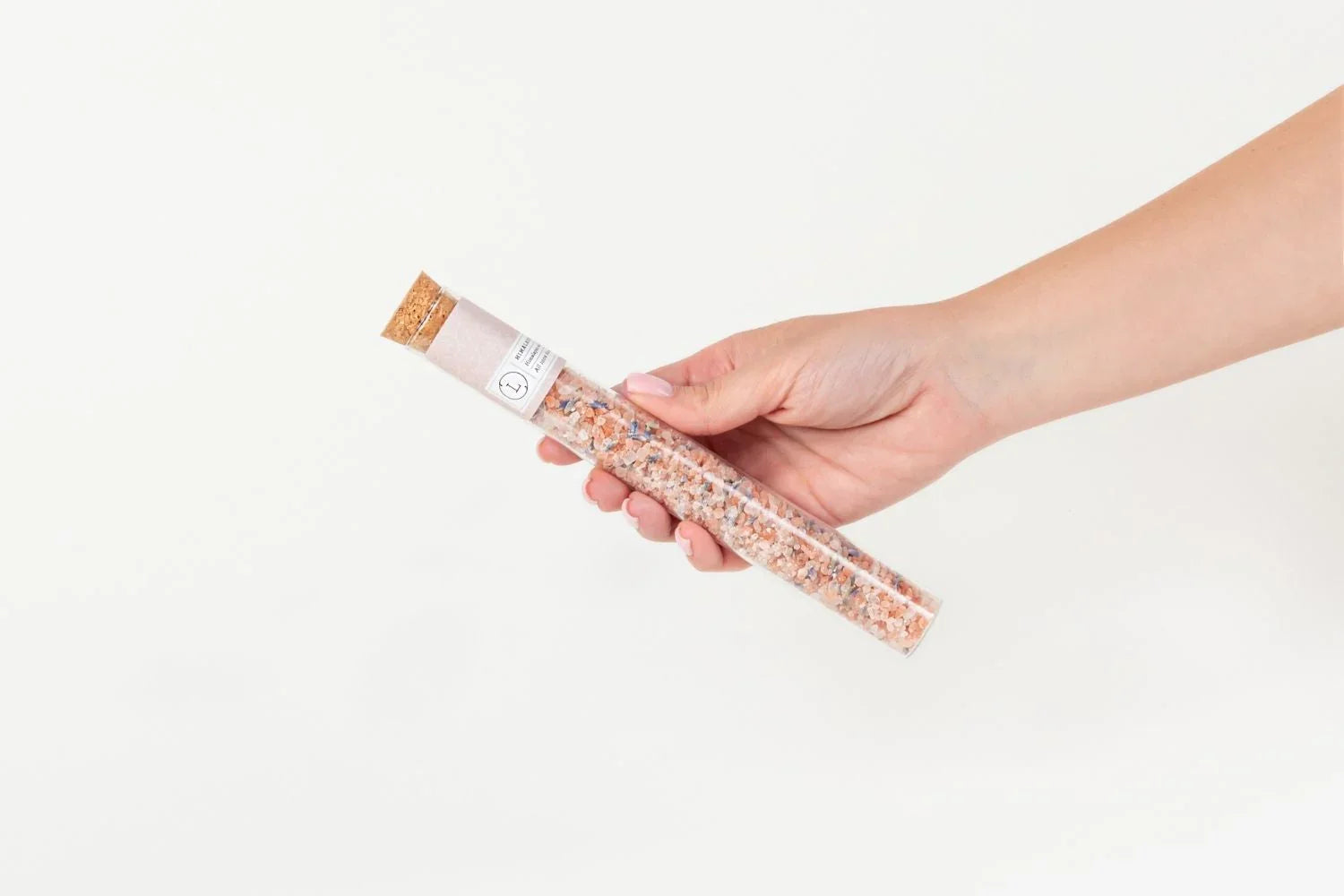 Hand holding a clear glass test tube filled with pink bath salt crystals and cork stopper