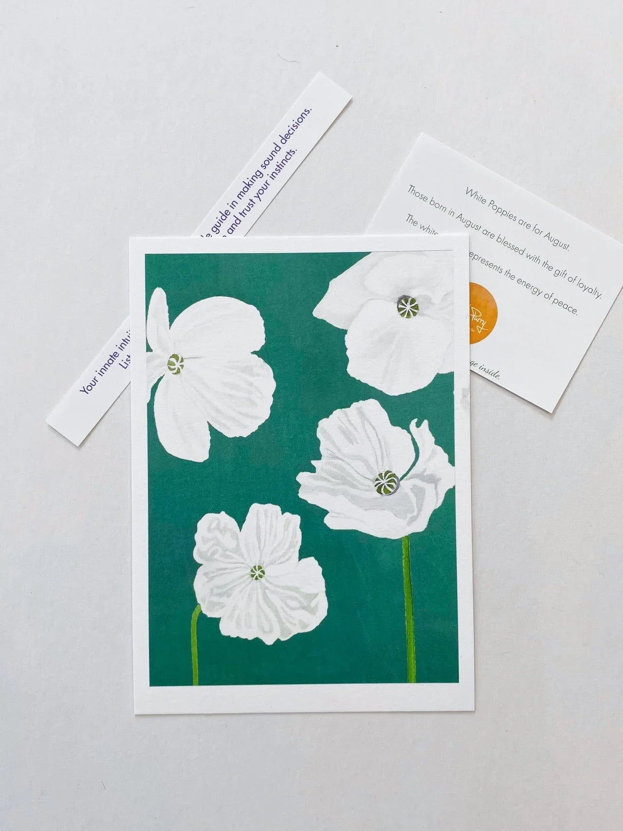 Art print featuring white poppies on teal background with informational cards about August birth month flowers