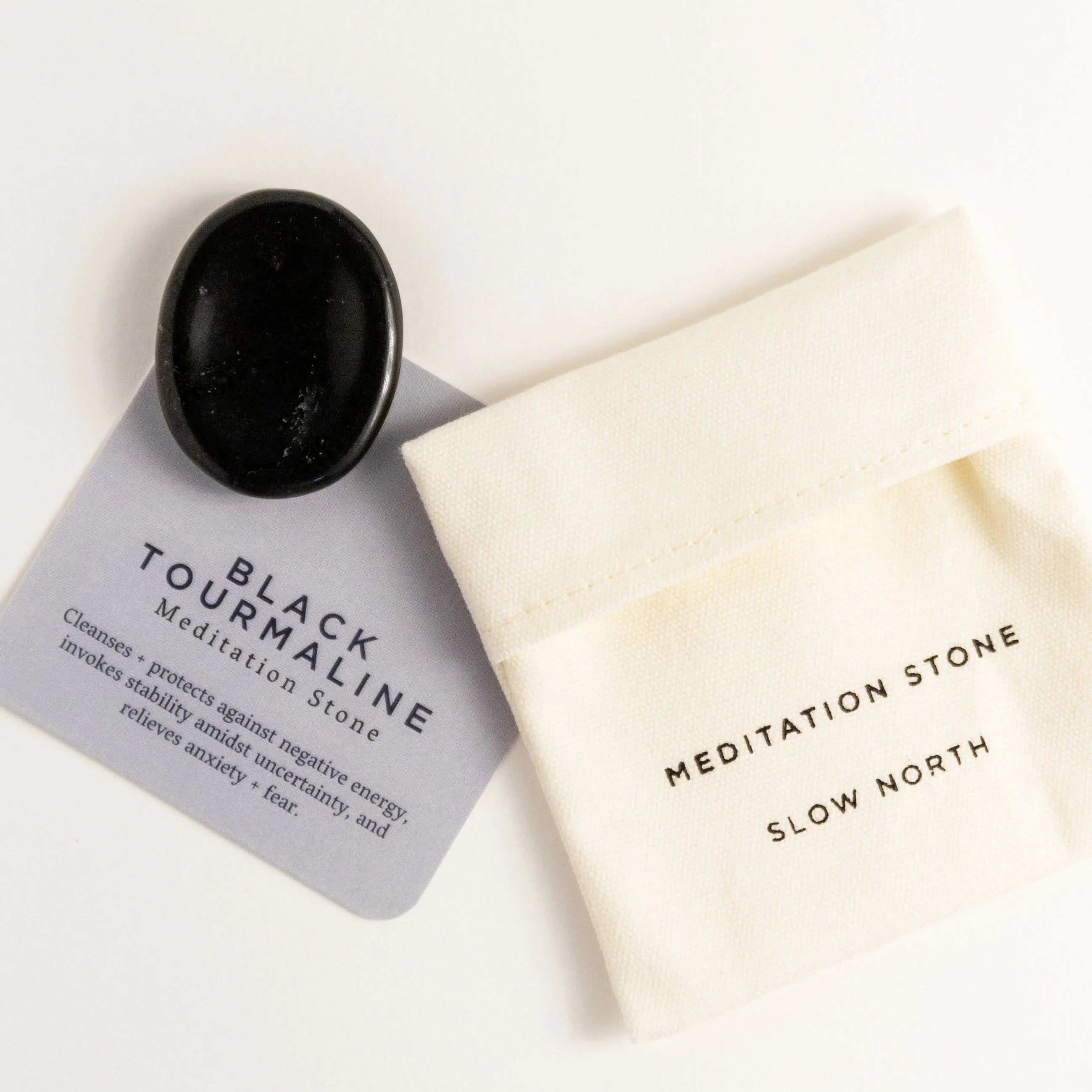 Polished black tourmaline meditation stone on card with benefits next to white cloth pouch