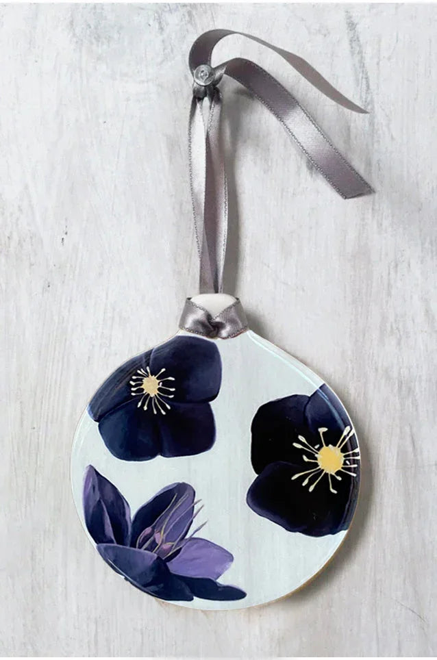 Round glass ornament with dark purple and black hellebore flower design hanging on gray ribbon