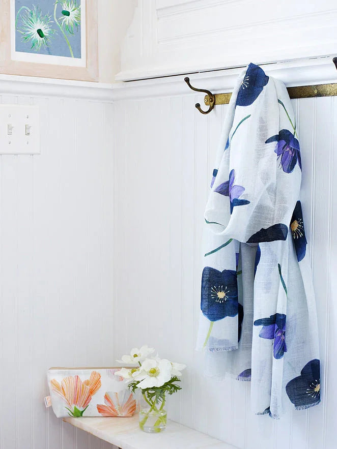 Light blue scarf with dark blue floral print hanging on brass hooks in bright white room