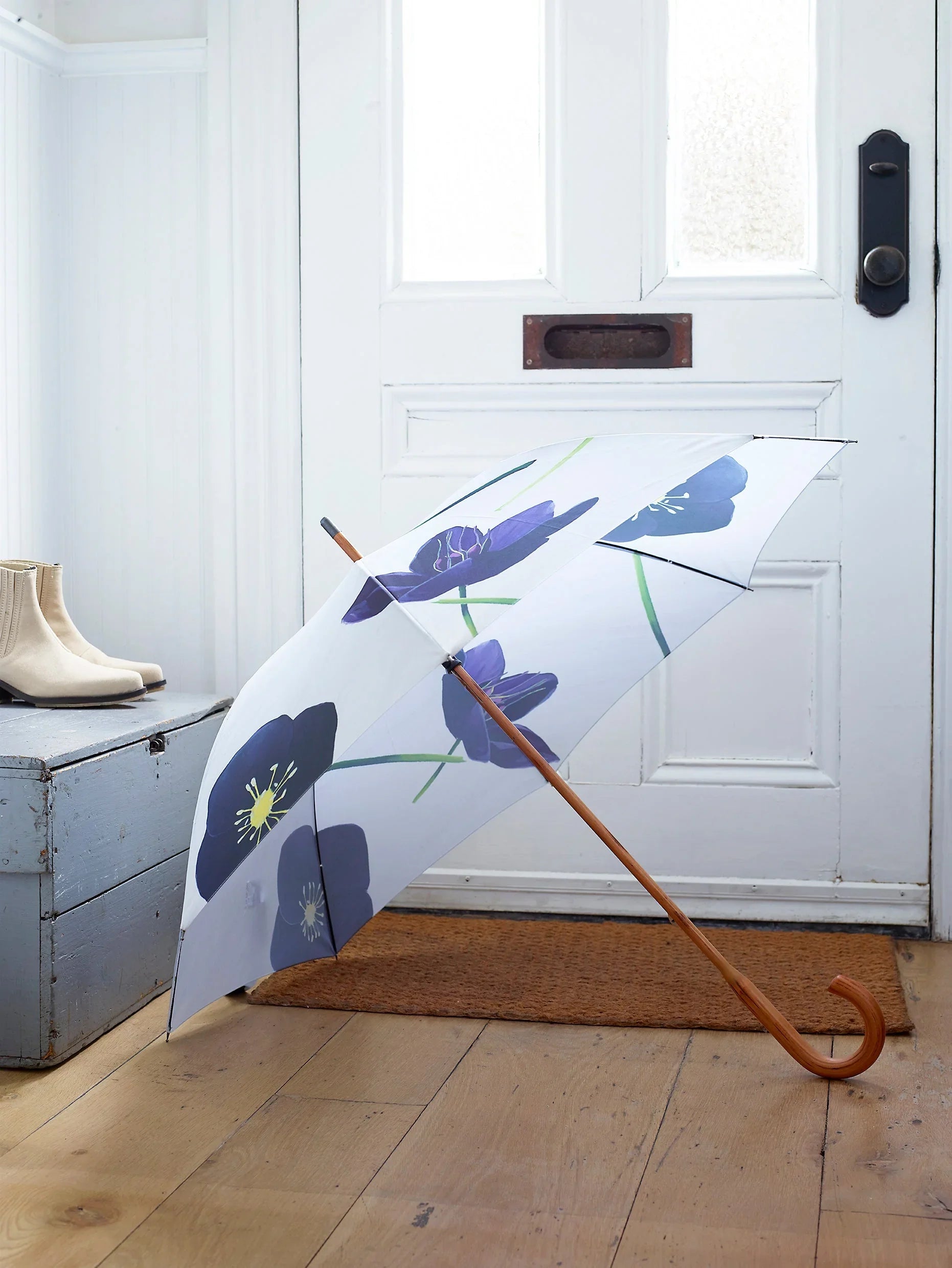 White umbrella with large blue floral pattern and wooden curved handle indoors on wooden floor