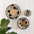 Artist-designed woven baskets with geometric patterns on white paneled wall, boutique decor