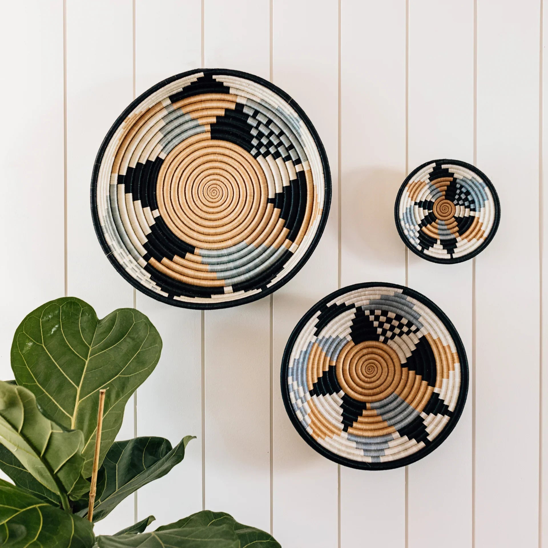 Artist-designed woven baskets with geometric patterns on white paneled wall, boutique decor