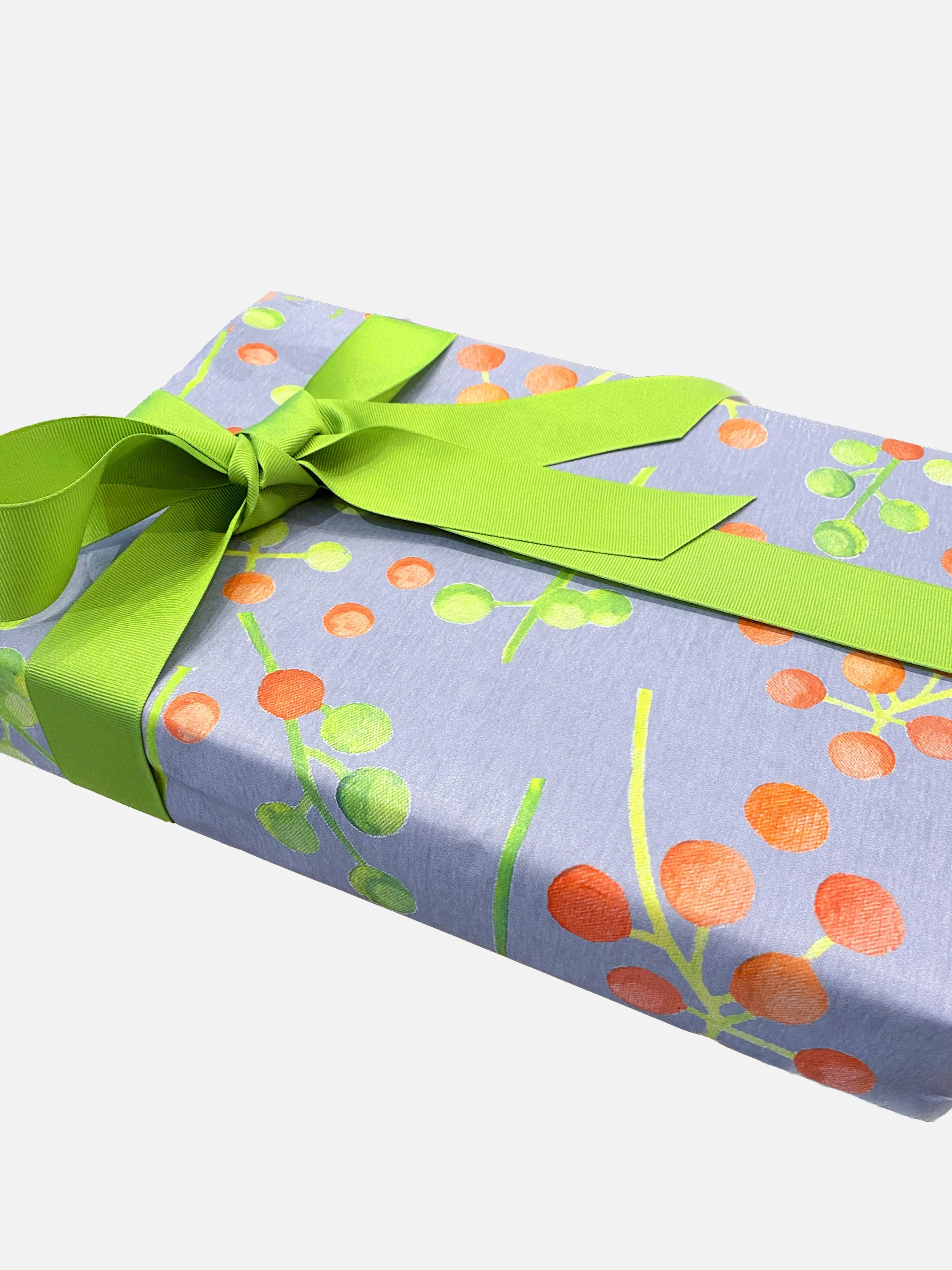 Gift box wrapped in botanical print paper with orange and green berries, tied with a bright green ribbon