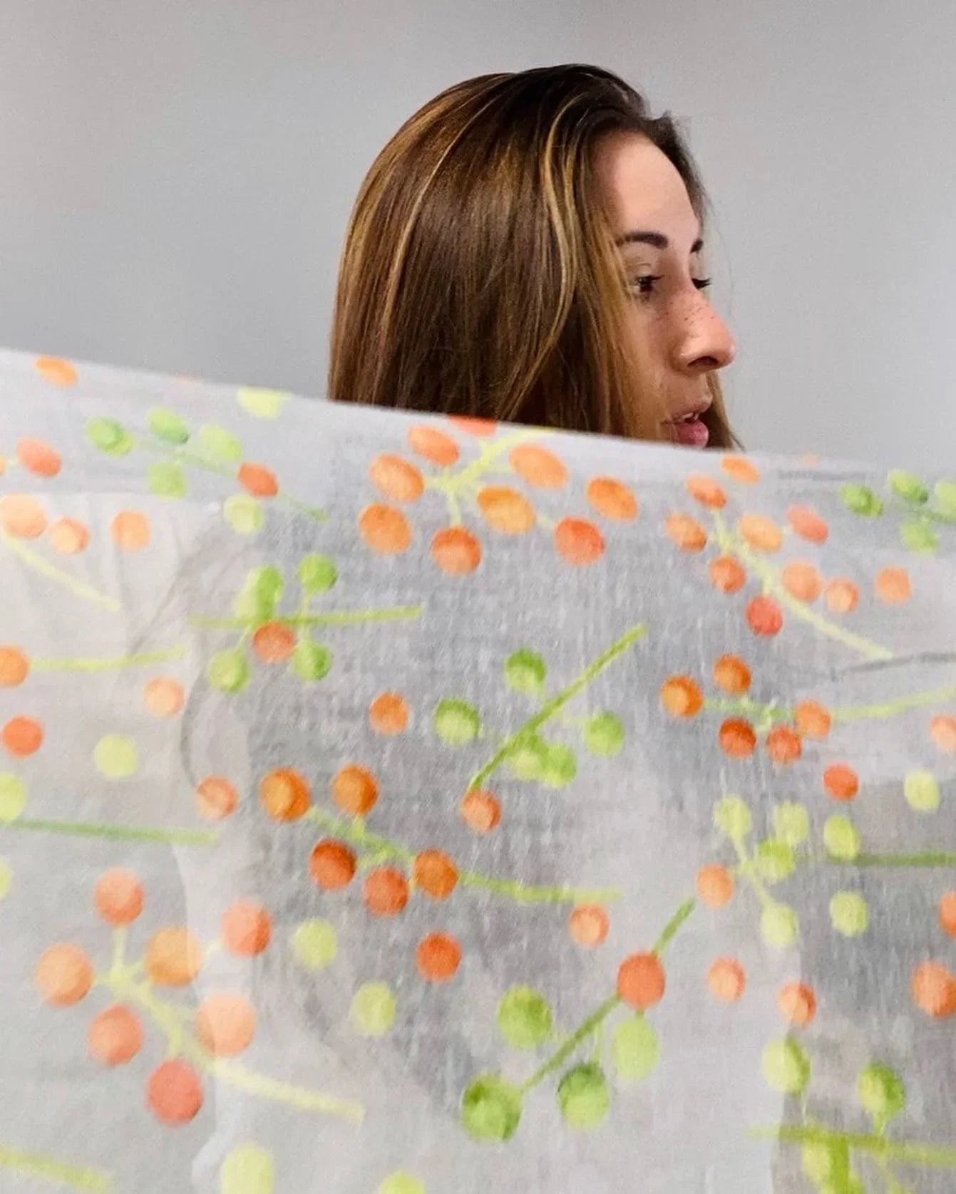 Woman with brown hair holding a sheer scarf with orange and green berry prints