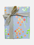 Gift box wrapped in blue paper with orange and green berry patterns tied with frayed beige fabric ribbon