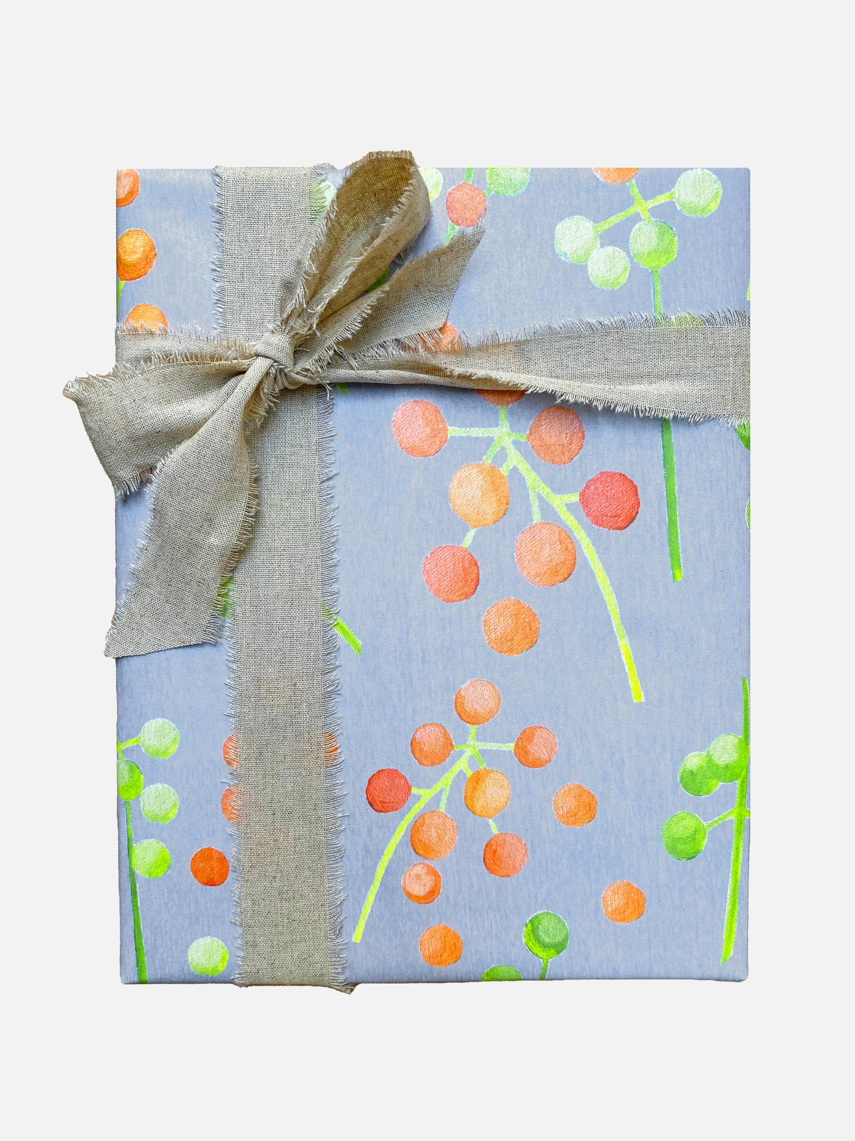 Gift box wrapped in blue paper with orange and green berry patterns tied with frayed beige fabric ribbon