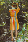 Person in colorful robe with eye and rainbow stripes motif standing in a lush green forest