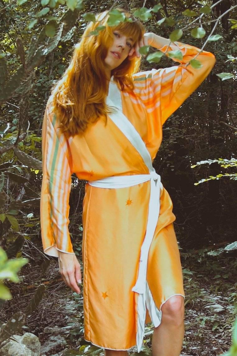 Woman in orange star-patterned kimono robe with white belt posing in green forest
