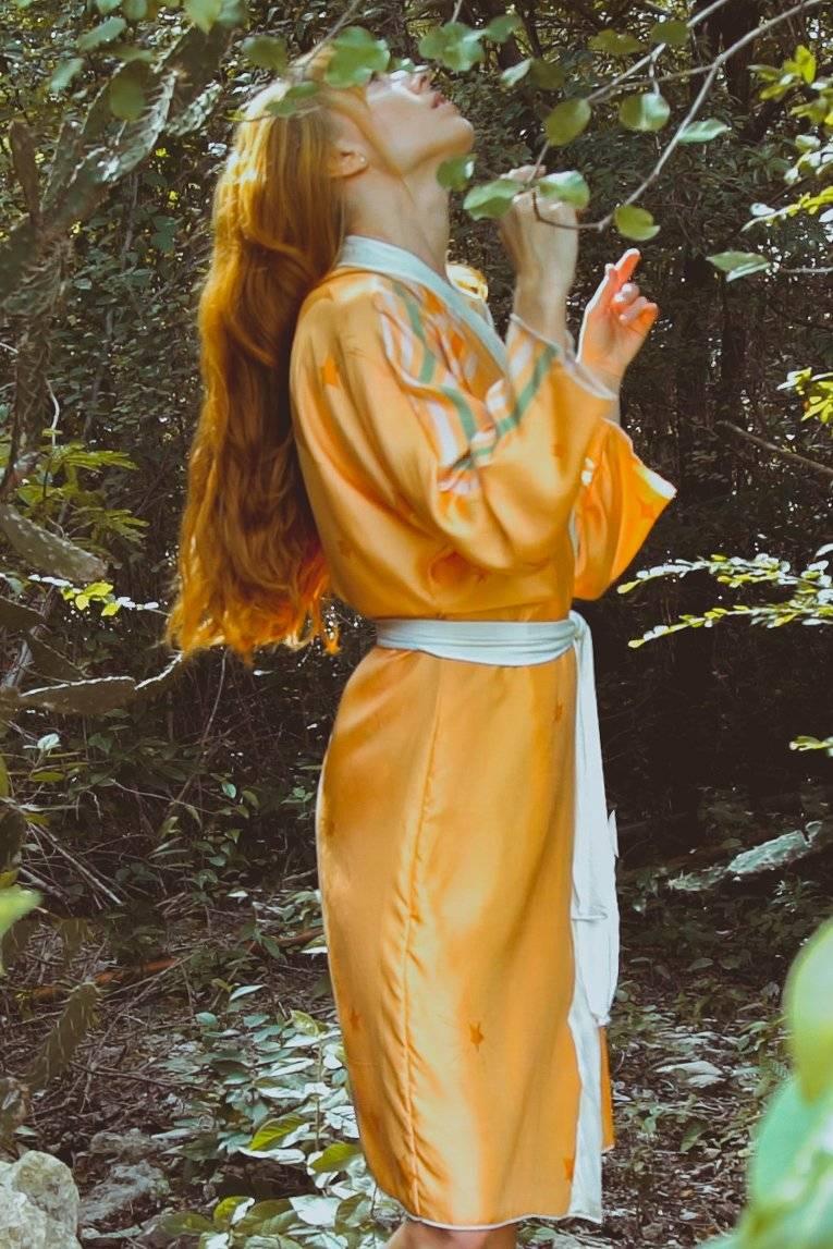 Woman with long red hair wearing a yellow satin robe with star patterns in a forest setting