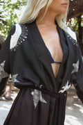 Close-up of a woman wearing a black kimono robe with white starfish patterns and a navy bikini top outdoors