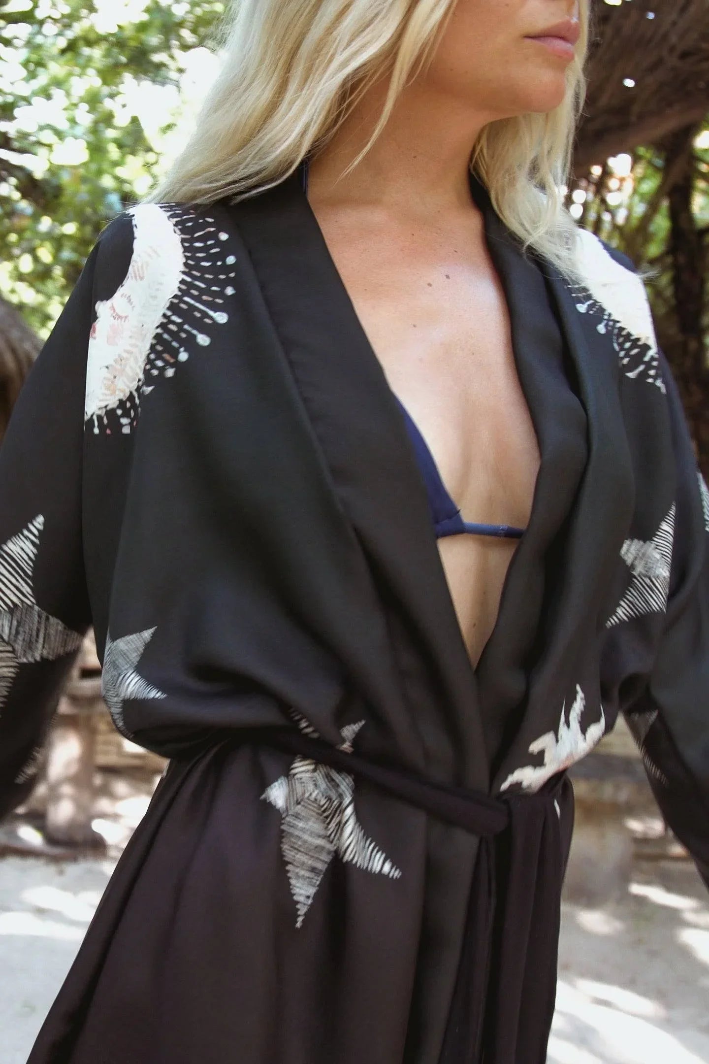 Close-up of a woman wearing a black kimono robe with white starfish patterns and a navy bikini top outdoors