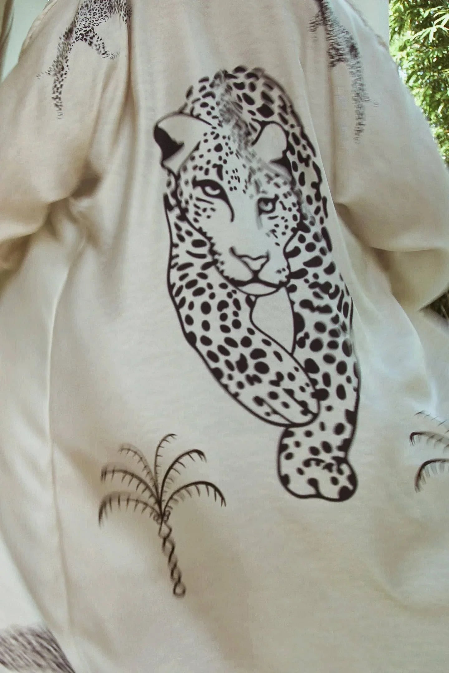 Cream-colored fabric with black leopard print and palm tree illustrations, outdoor background