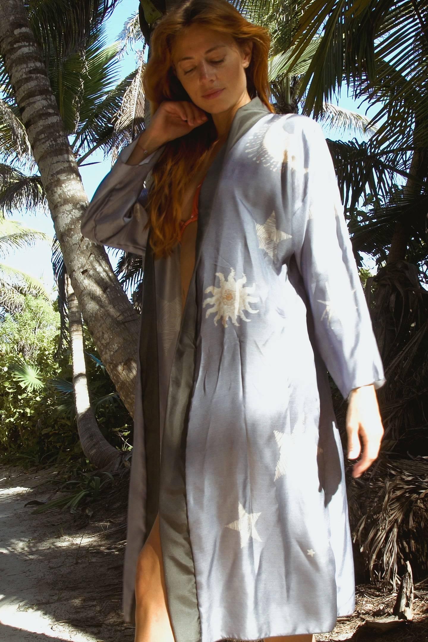 Woman in a light gray robe with sun and star patterns standing in a tropical palm tree setting